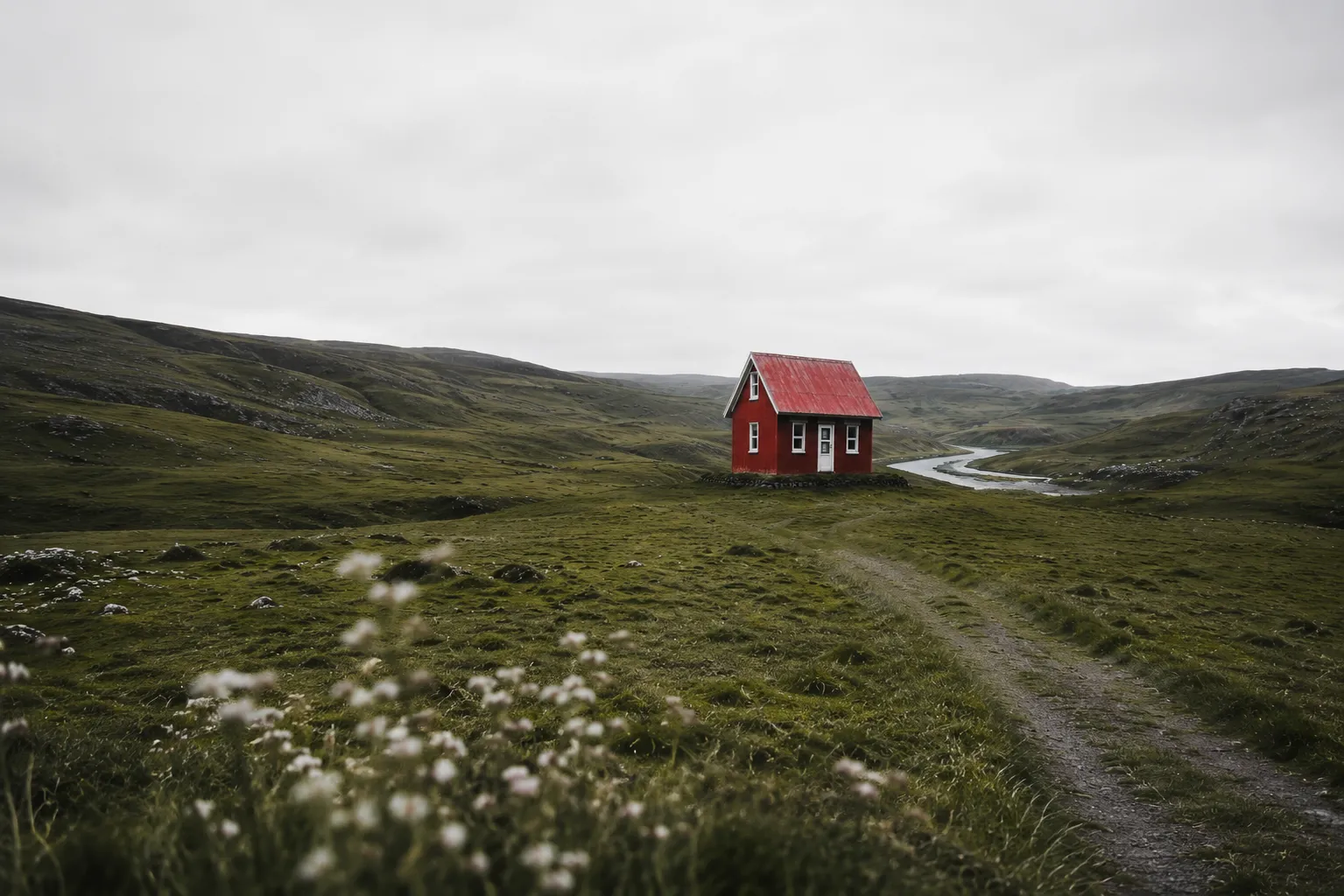 Rustic red chalet photographed from the side, surrounded by rolling green hills and remote mountain landscapes.