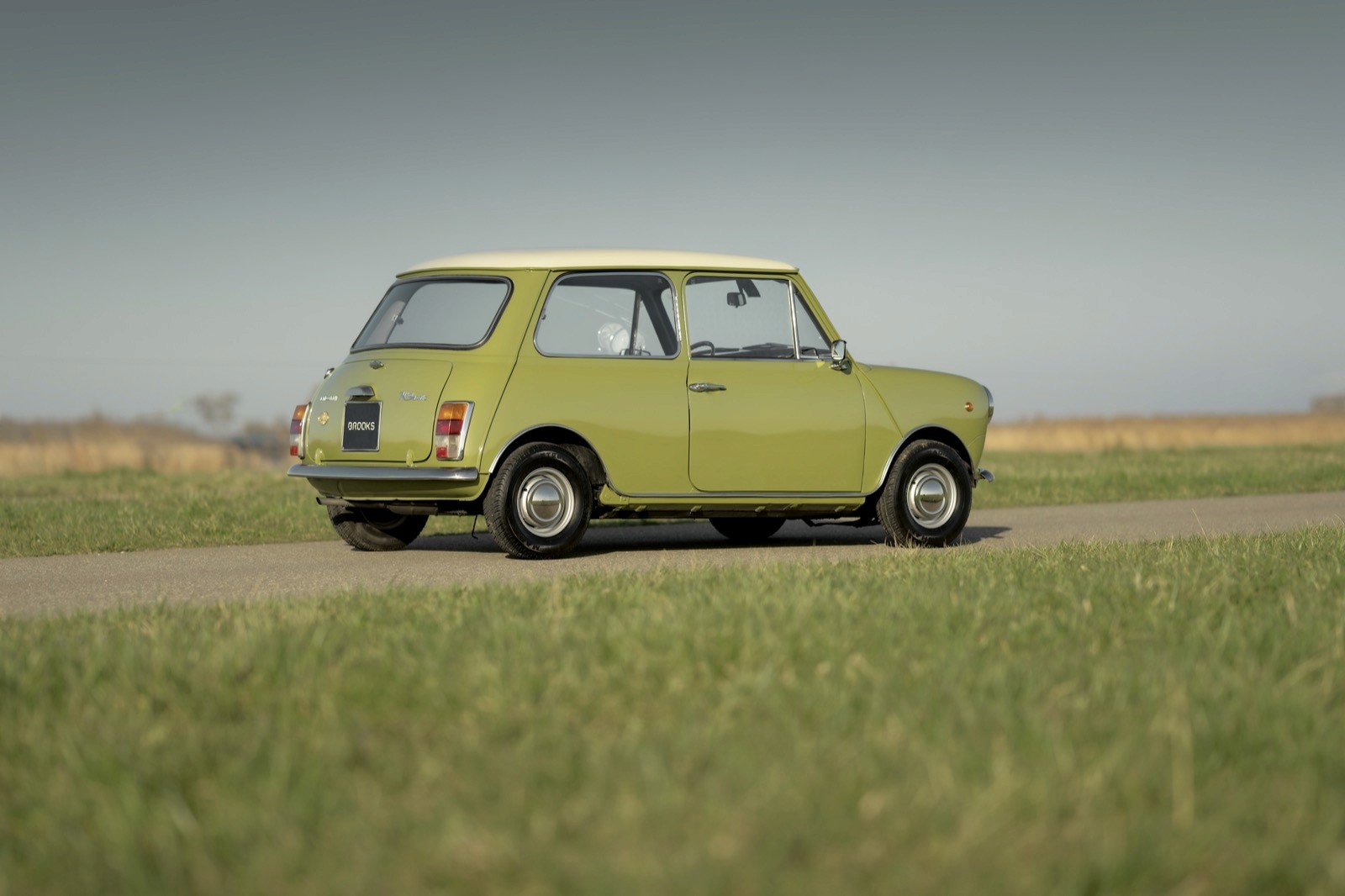 A vintage lime green car parked on a gravel road surrounded by open fields under a clear sky.