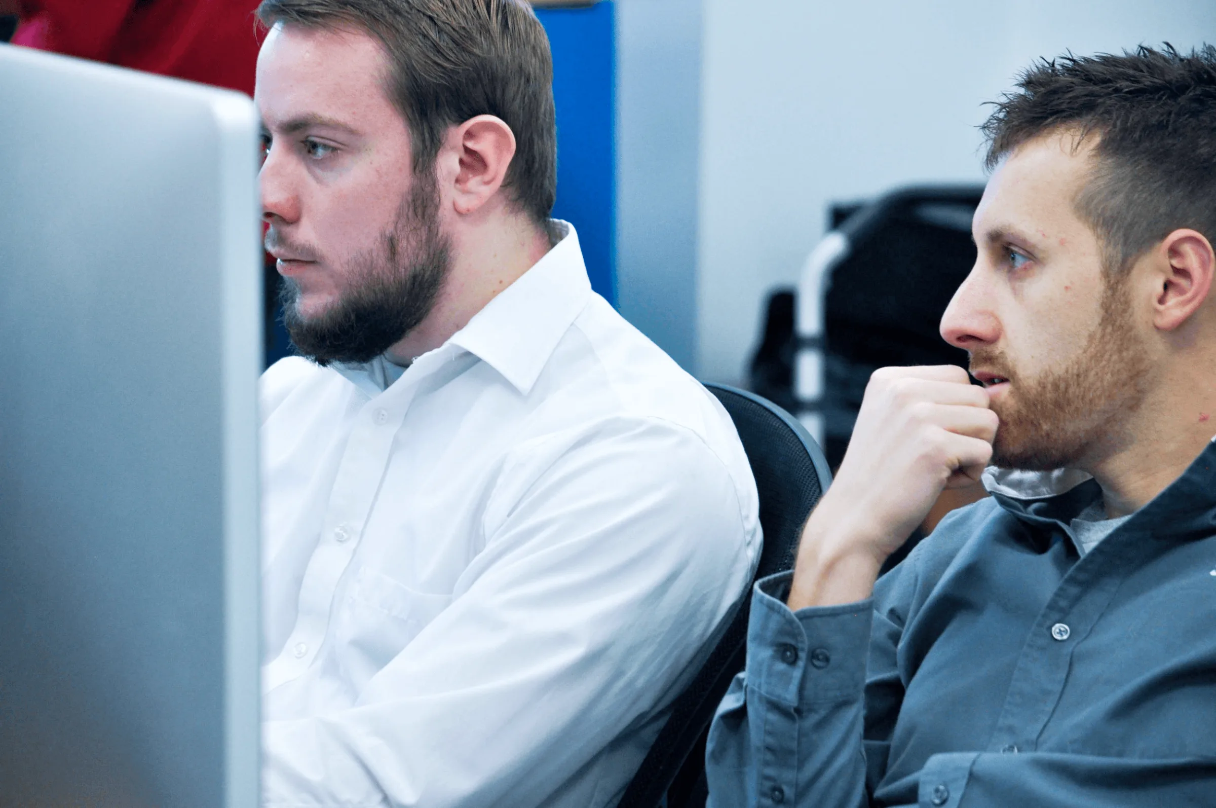 Two developers intently reviewing code together on a monitor in an office setting.