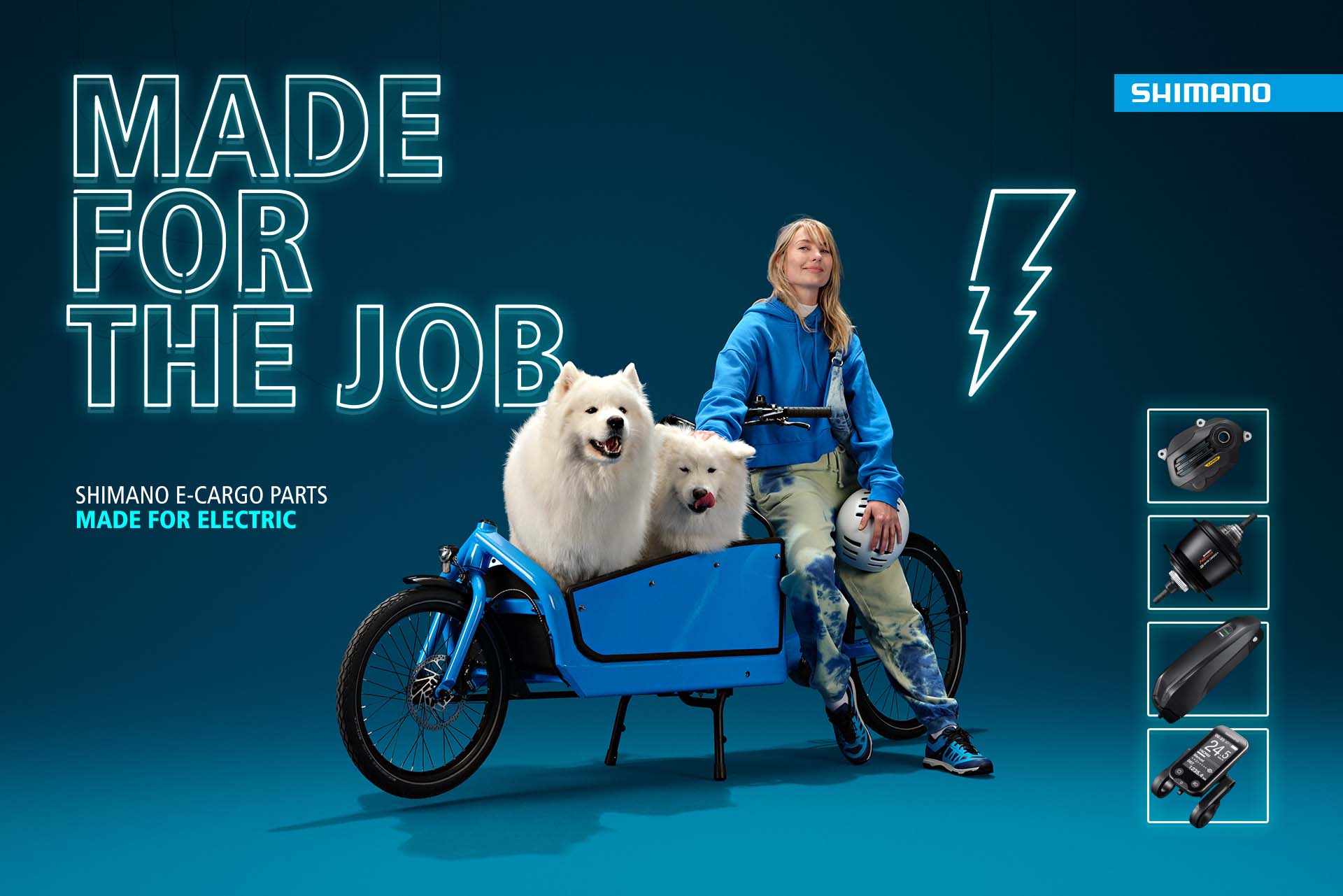 Woman in a blue hoodie seated on a blue Shimano e-cargo bike with two white fluffy dogs in the cargo box, against a deep teal "Made For The Job" backdrop.