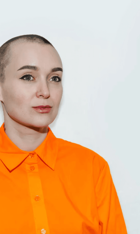 Portrett av designer Kristin Skårdal, ikledd orange skjorte på lys blåhvit bakgrunn