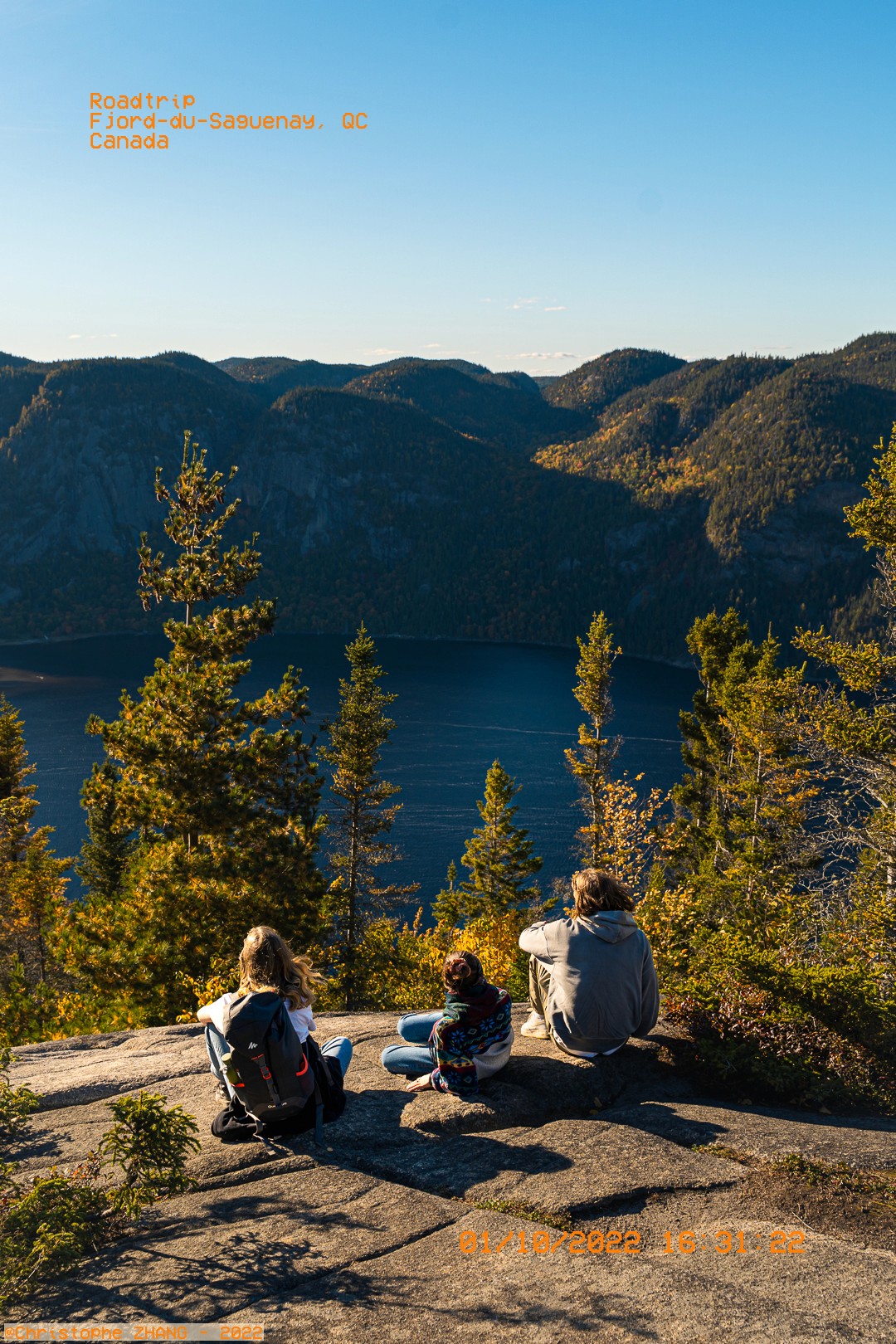 Trois personnes profitant d'une vue panoramique sur le fjord du Saguenay en pleine nature.
