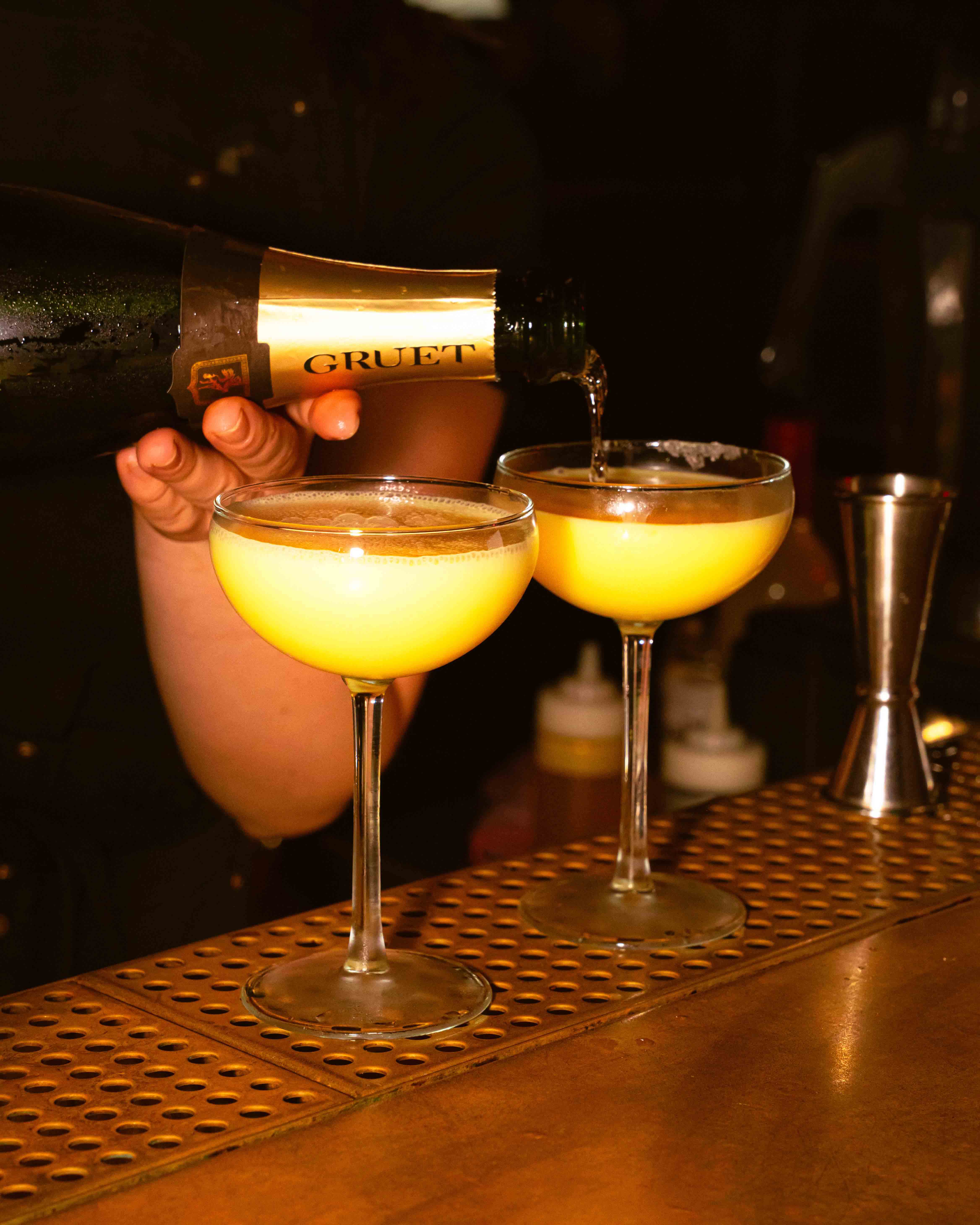 Restaurant interior with wooden tables and chairs lined against a textured wall, softly lit by round wall lamps.