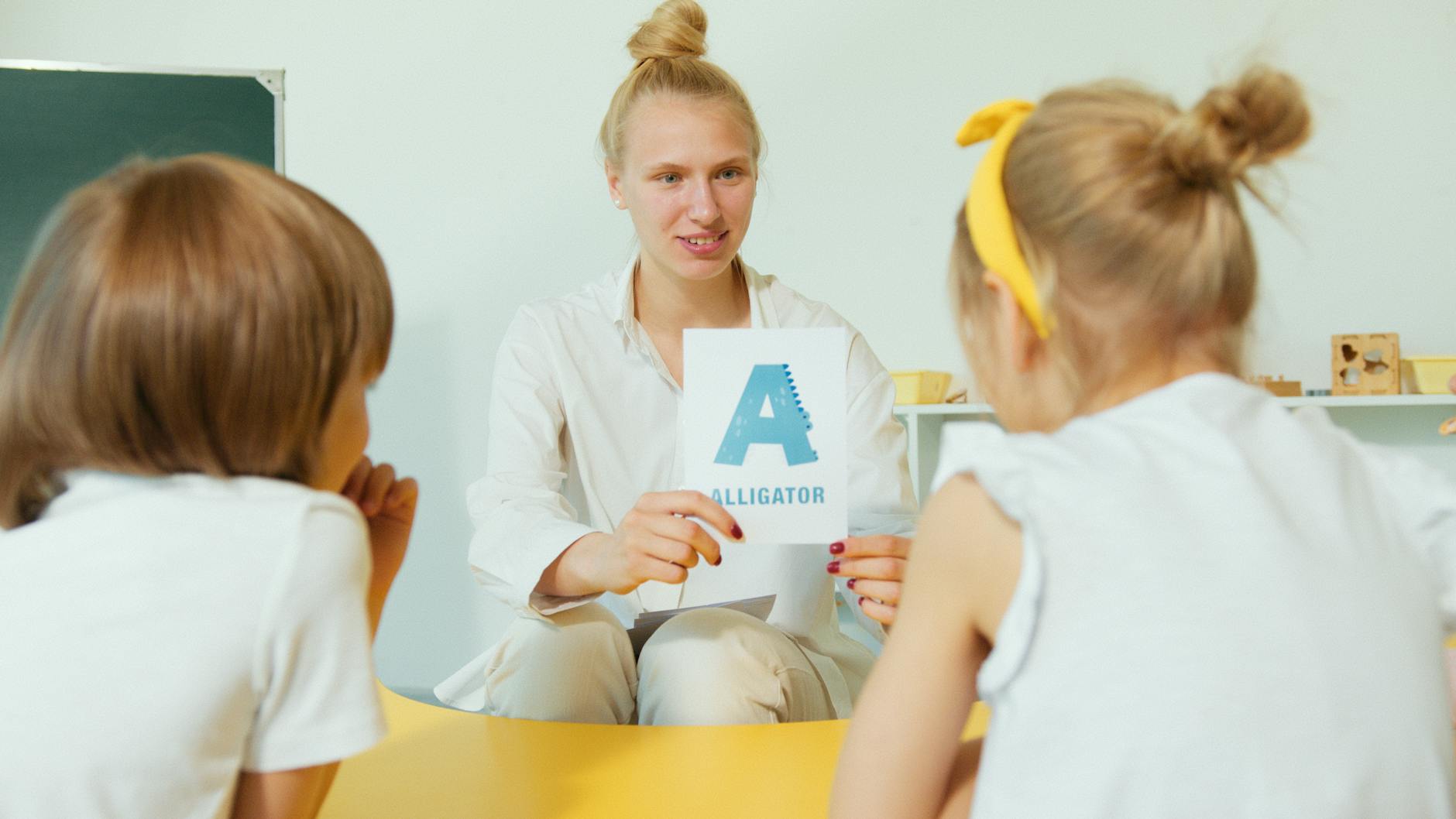 A reading teacher points to phonics patterns on a whiteboard while primary students watch attentively.