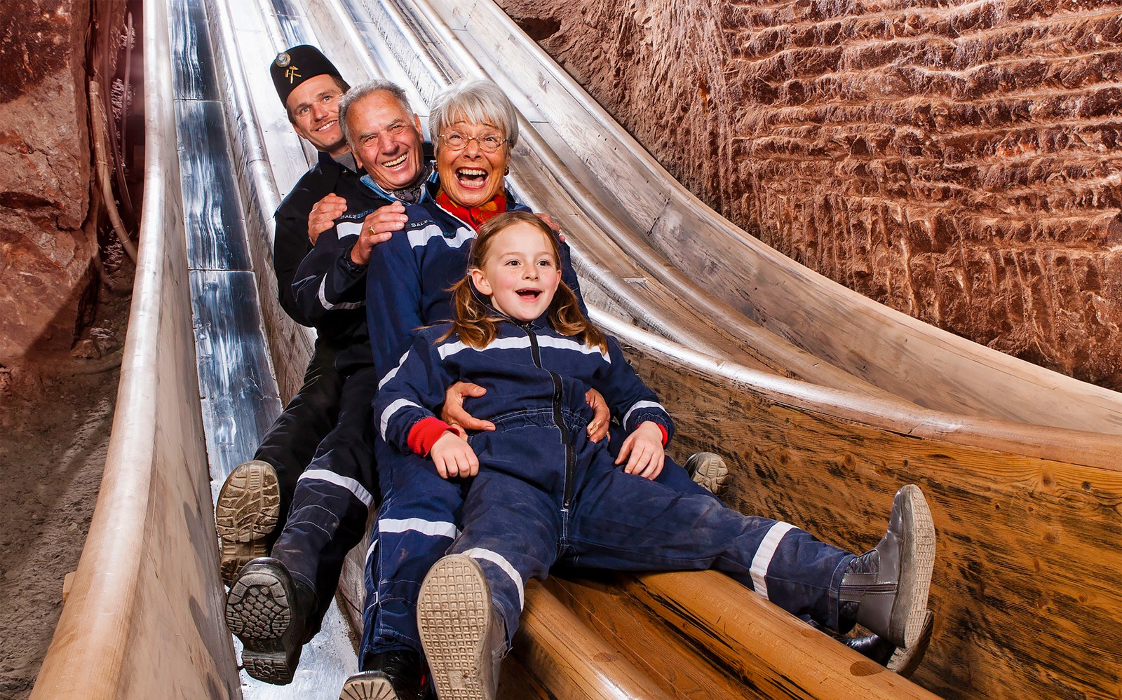 Besøgende glider ned ad en træskakt i en bayersk saltmine, Berchtesgaden-tur fra Salzburg.