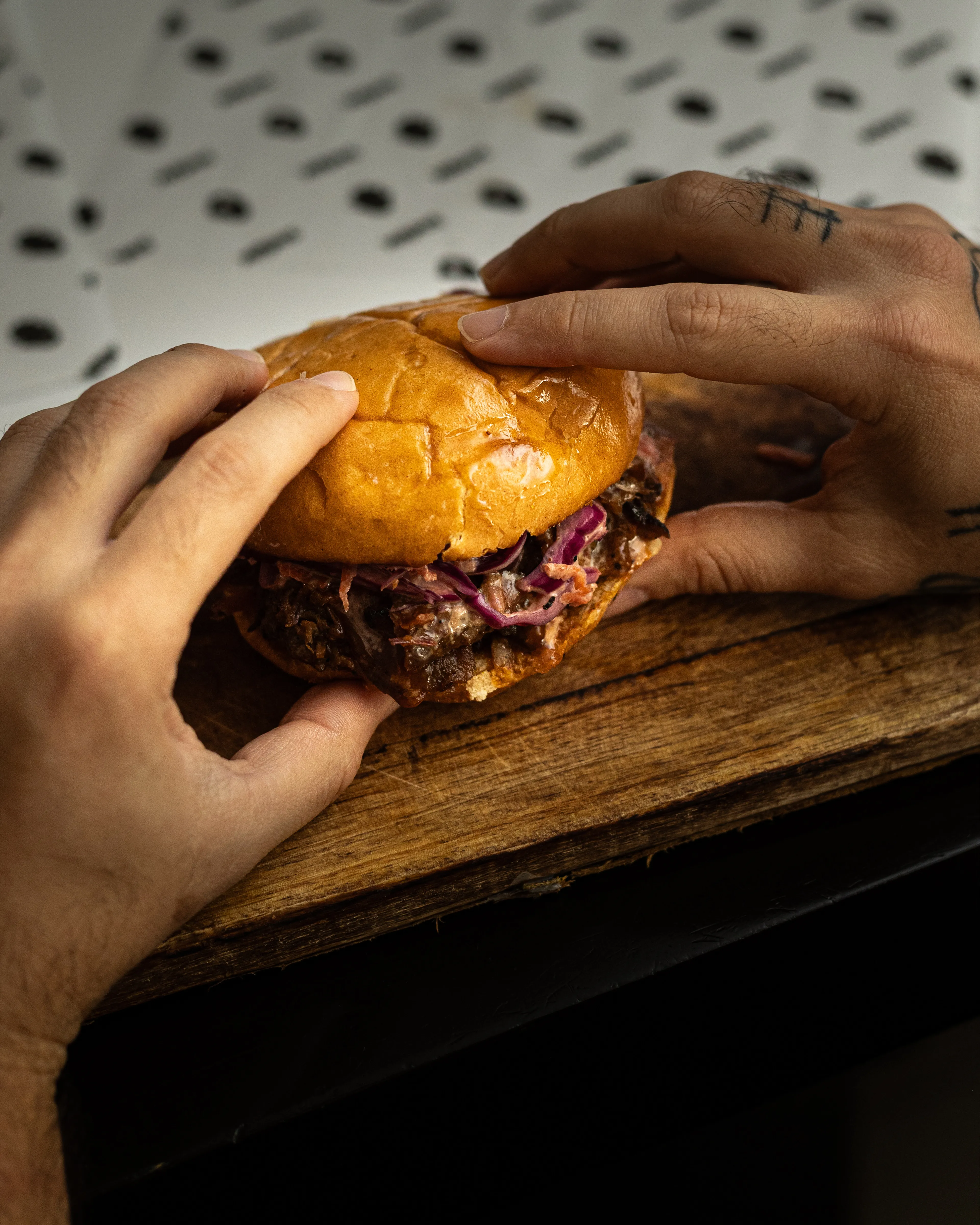 Manos sosteniendo hamburguesa de pulled pork Smük sobre tabla de madera.