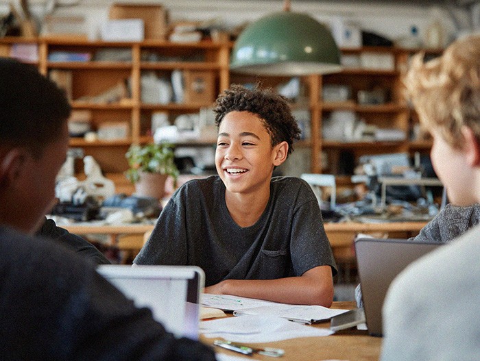 “Student smiling while collaborating with classmates around a table in a classroom.