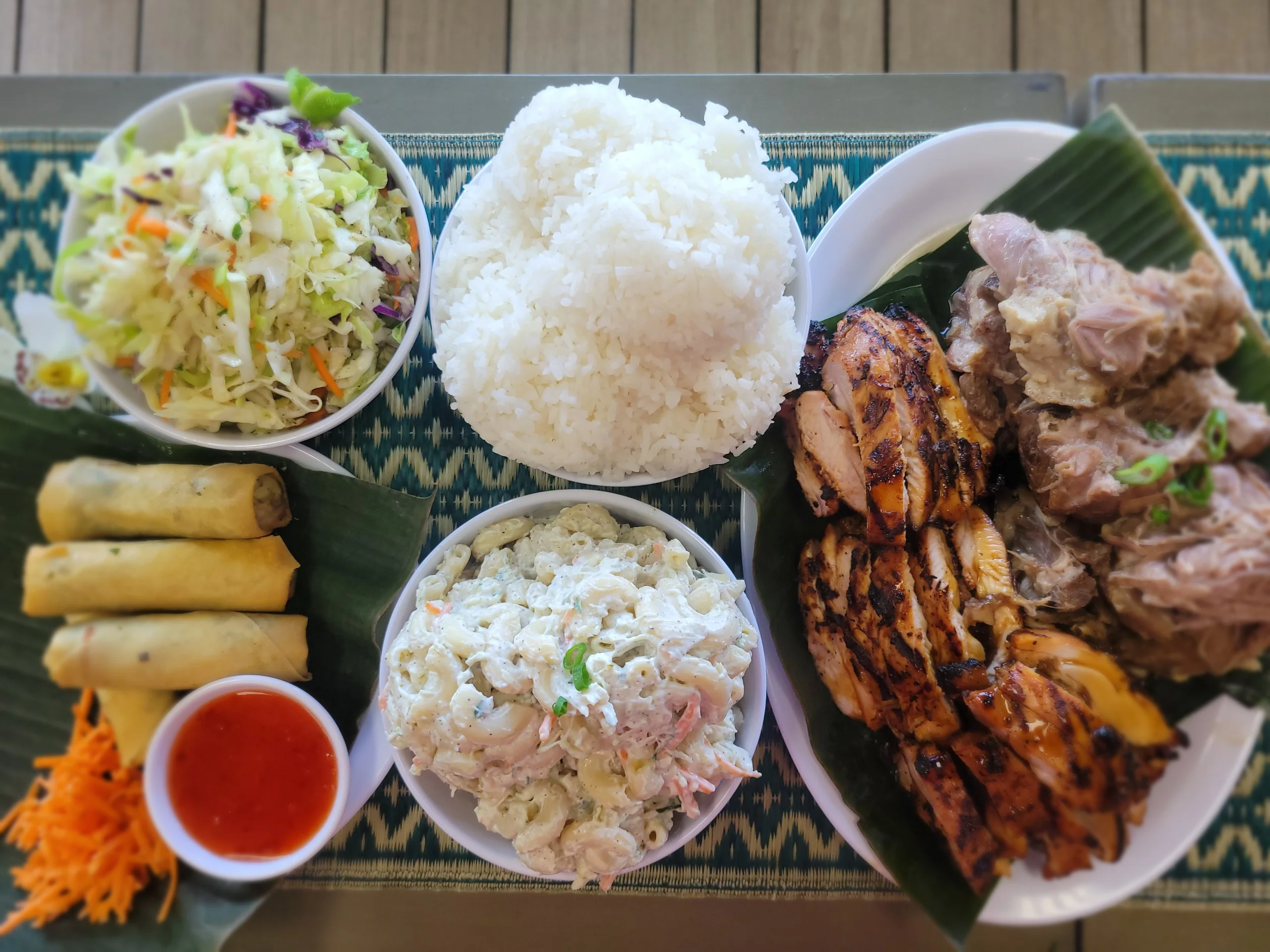A large family-sized Hawaiian mix plate featuring grilled meats, rice, macaroni salad, and spring rolls.
