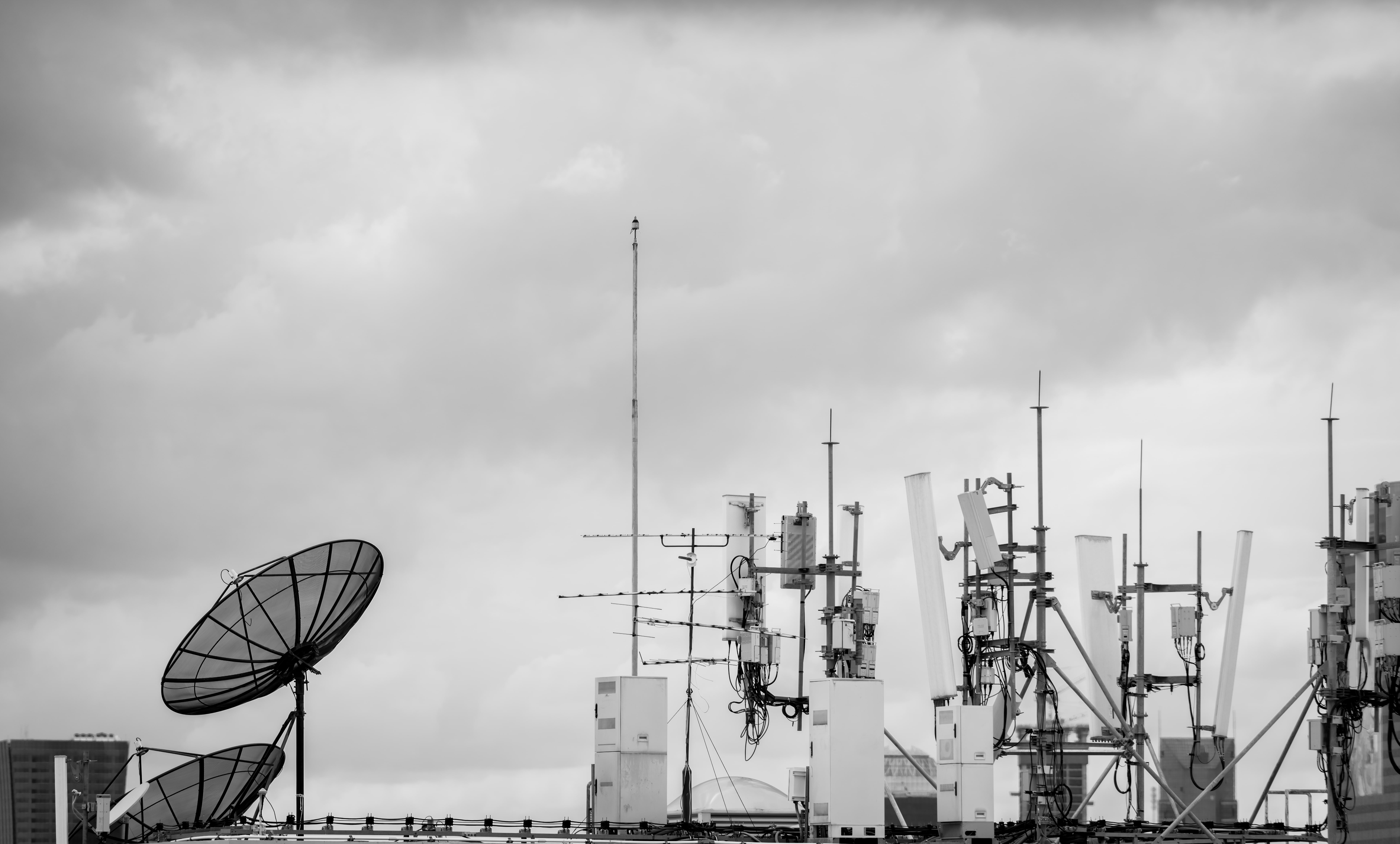 5G telecommunication antennas and satellite dishes on rooftop under cloudy sky