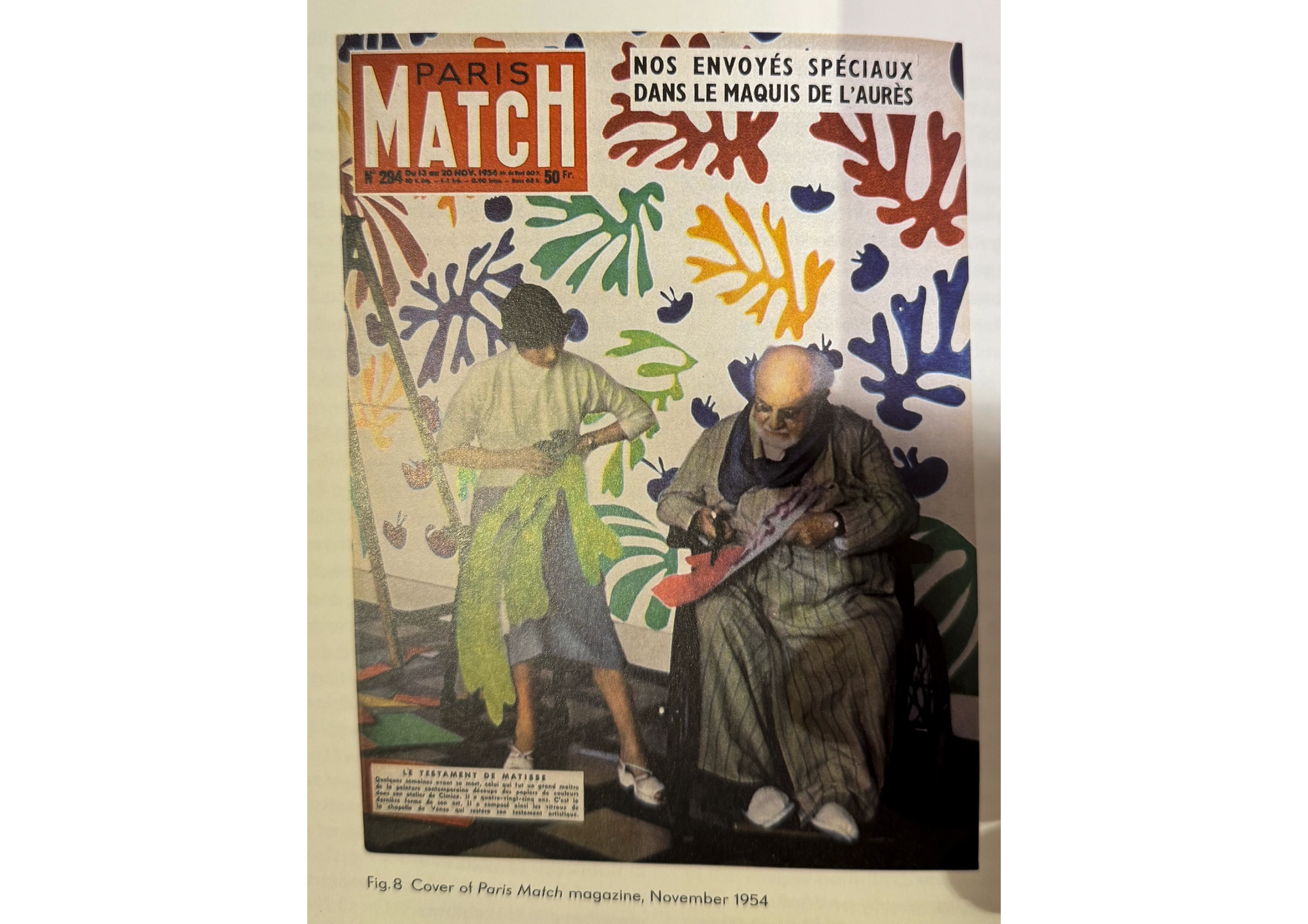 Magazine cover showing Henri Matisse in a wheelchair cutting shapes from paper, seated before a wall of cut-out leaf forms, with a younger woman standing beside him.