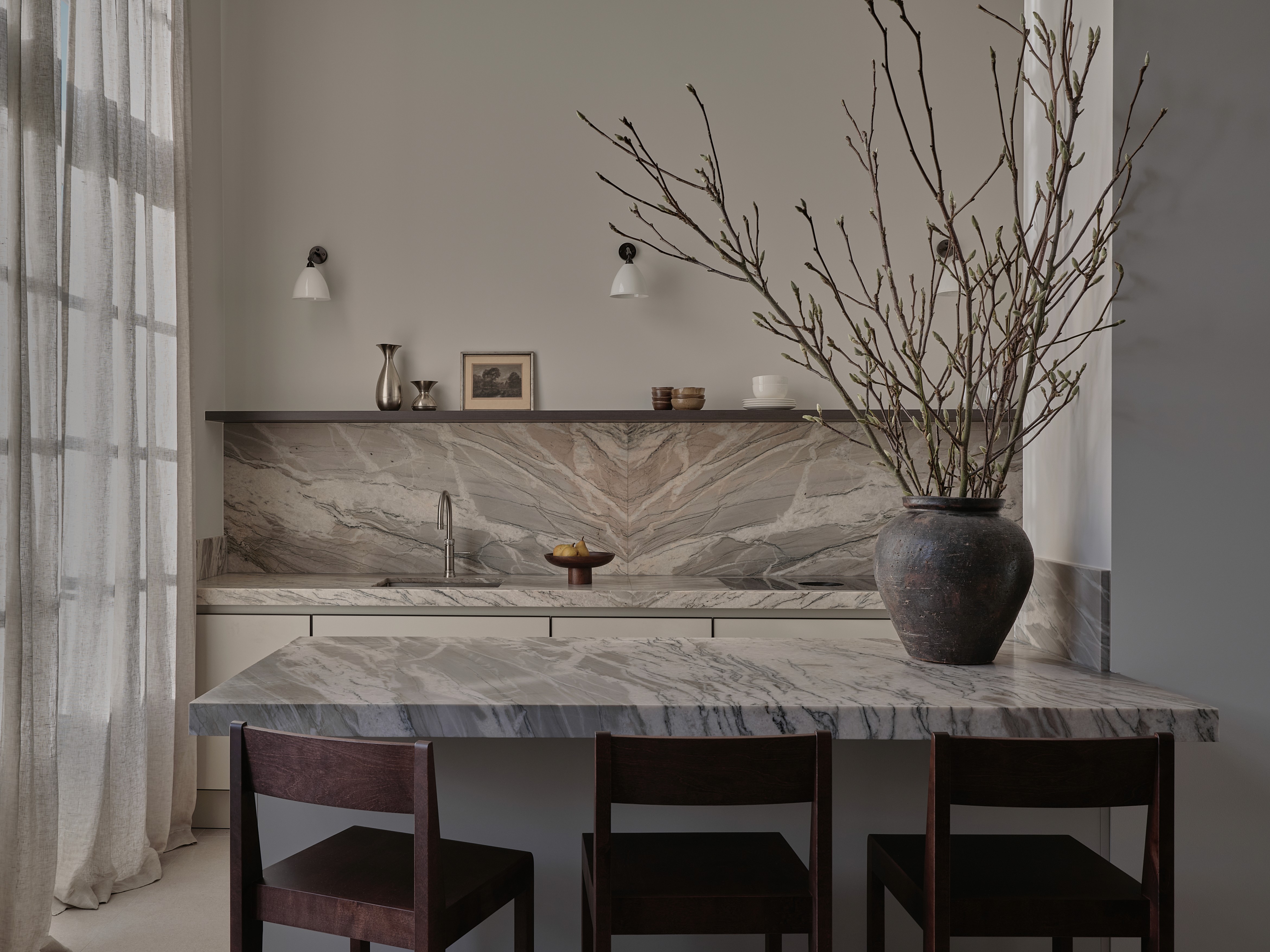 The Residence project - Bespoke kitchen with book-matched quartzite backsplash and island, dark wood bar stools, dark oak open shelving, white ceramic sconces, and vintage vases