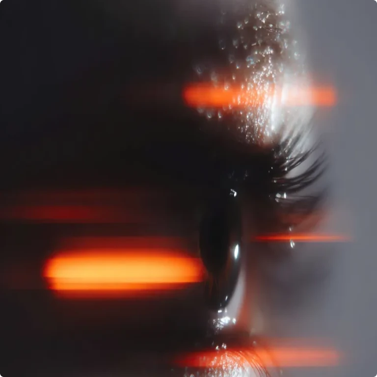 Close-up of a human eye with long eyelashes and blurred orange lights.