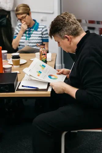 Person sitting at a table writing with papers and cups.