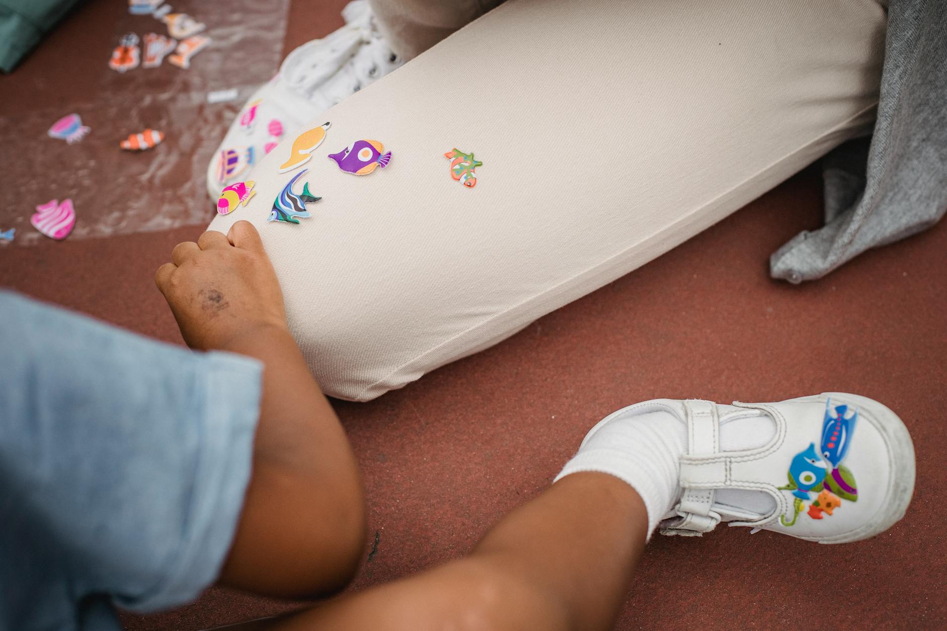 A young child using a finger to trace a felt maze in a sensory-rich activity book on a wooden table.