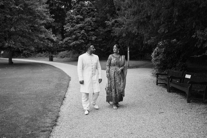 Black and white photo of a couple walking hand in hand along a curving path in Towneley Park