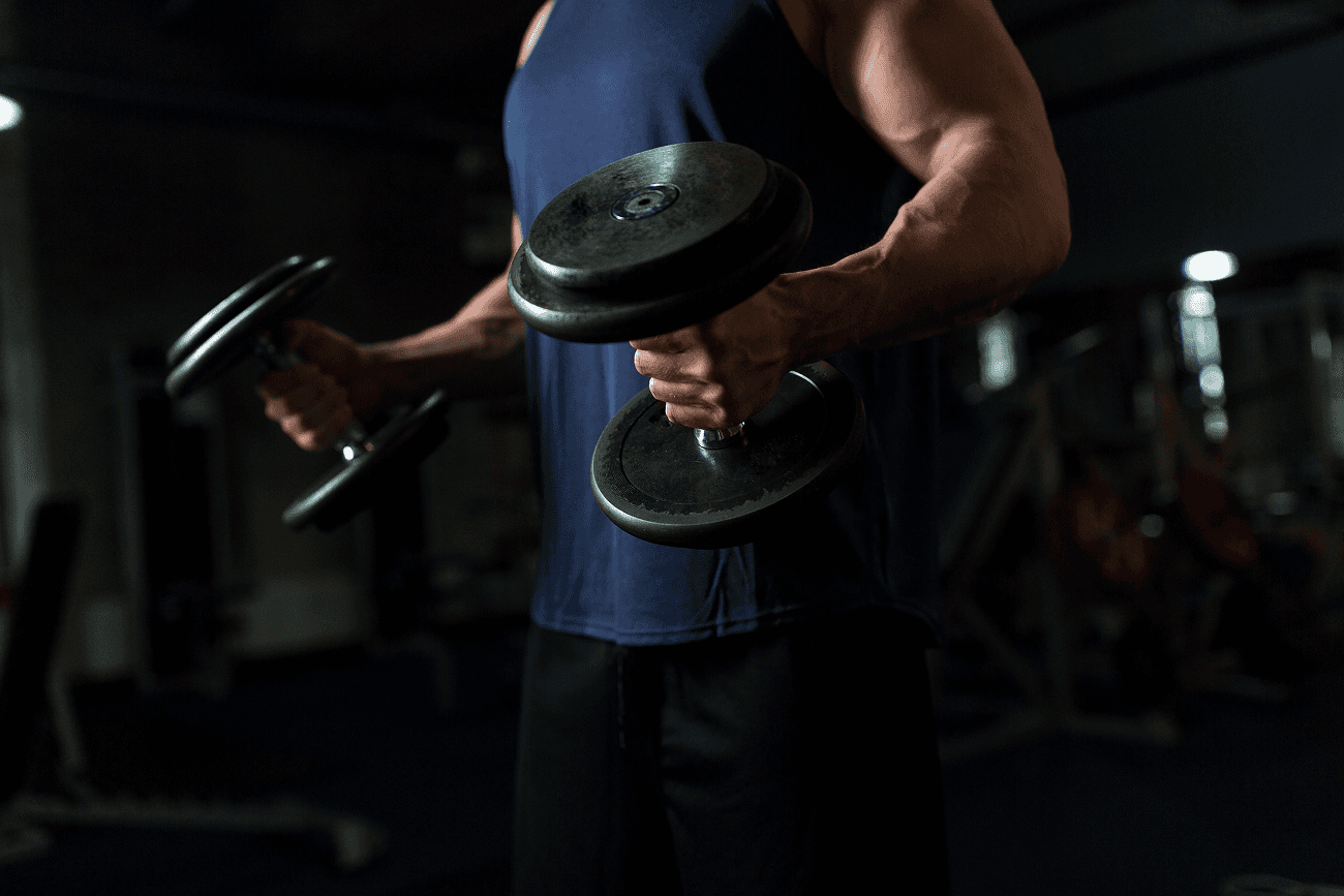 Close-up of a man lifting dumbbells in a dimly lit gym.