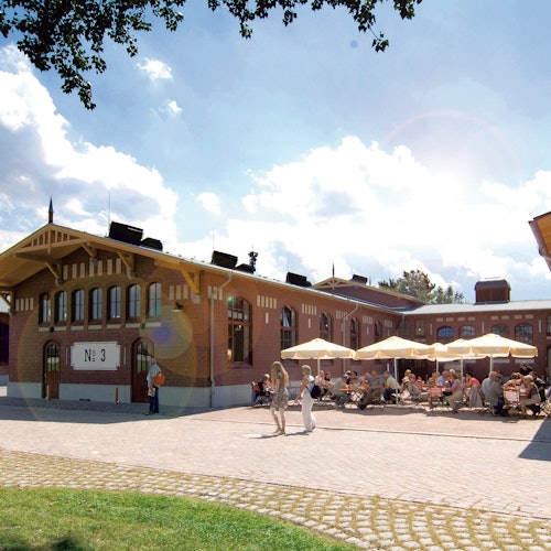 A sunny courtyard with people sitting under umbrellas at tables, adjacent to a historical brick building labeled "No. 3."
