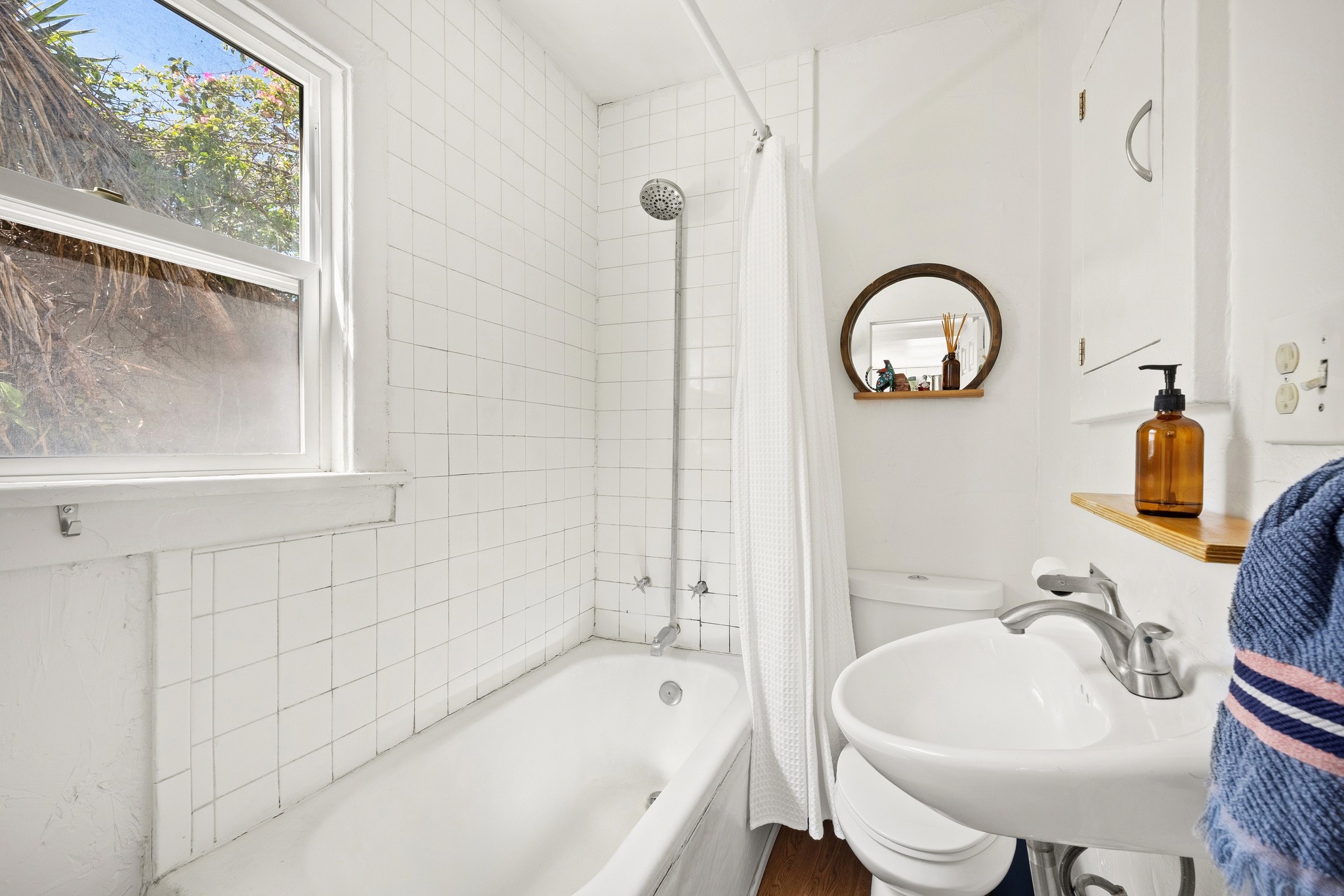 Bright bathroom at 3456 plata, featuring a bathtub, sink, and a round mirror, with a window allowing natural light.