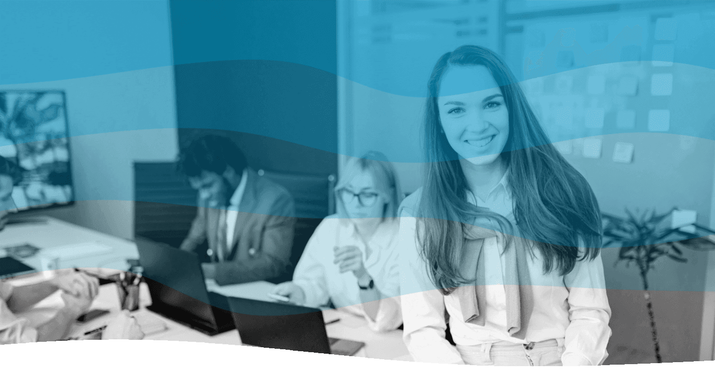 A group of professionals is working in a modern office, with a smiling individual in the foreground and colleagues collaborating on laptops in the background.