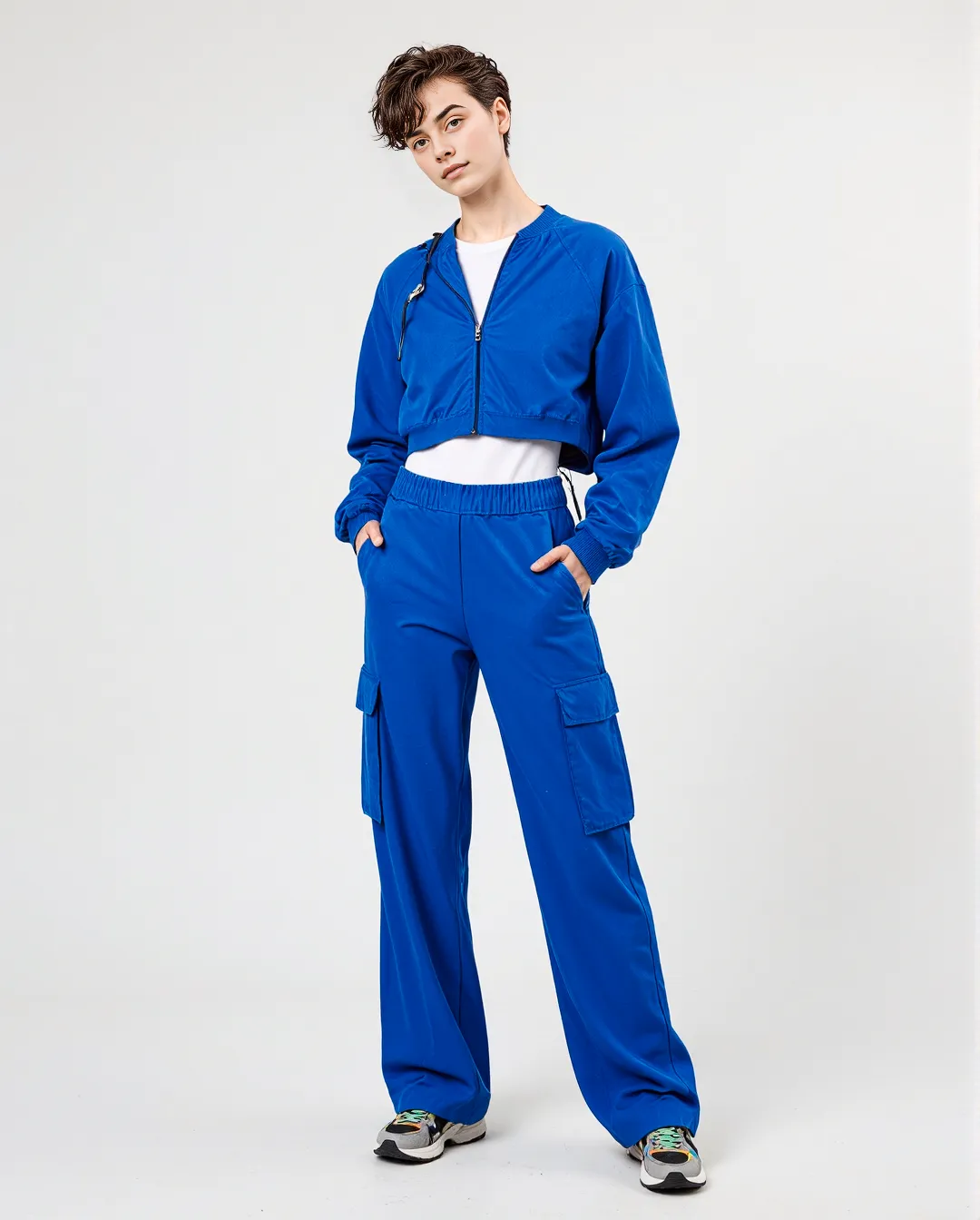 Modern cobalt blue athleisure set featuring a cropped zip-up jacket and wide-leg cargo pants against a minimalist white background