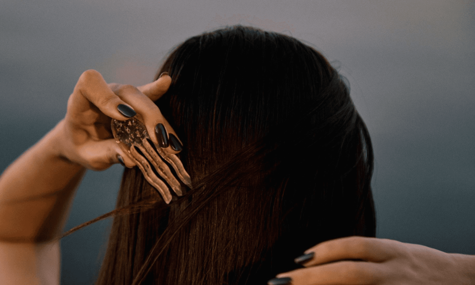 A person with long dark hair brushes their hair using a skeletal-themed comb against a muted background, showcasing a unique accessory.