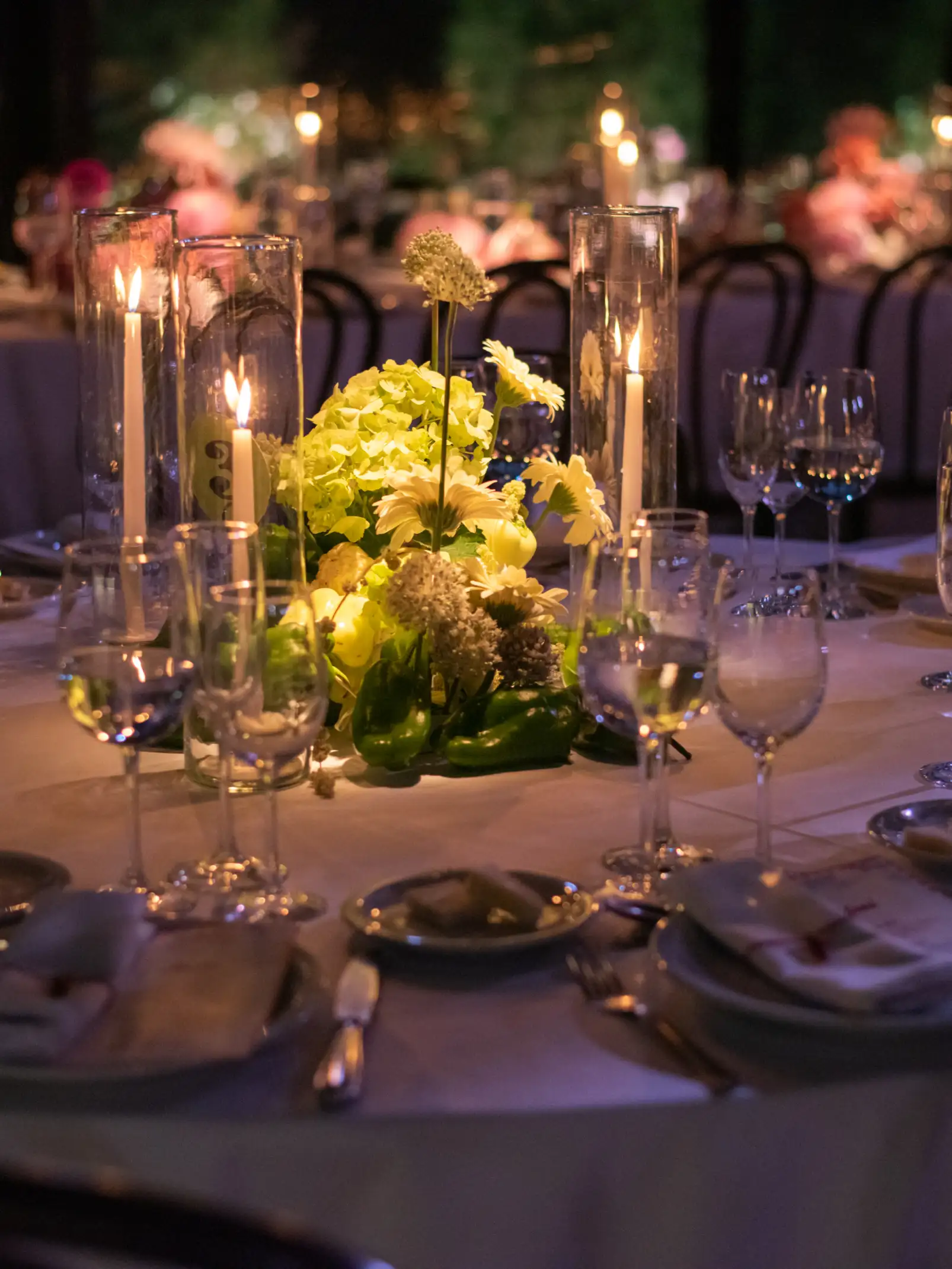 Mesa iluminada con velas altas y centro floral en tonos verdes y blancos para ambientación nocturna elegante.