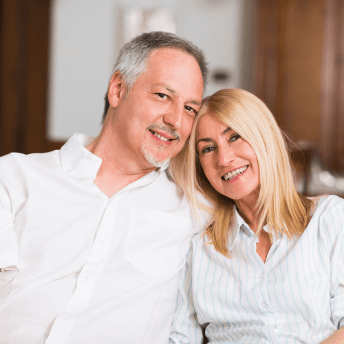 Portrait of a man with short hair and a beard, smiling in bright natural light against a white background.