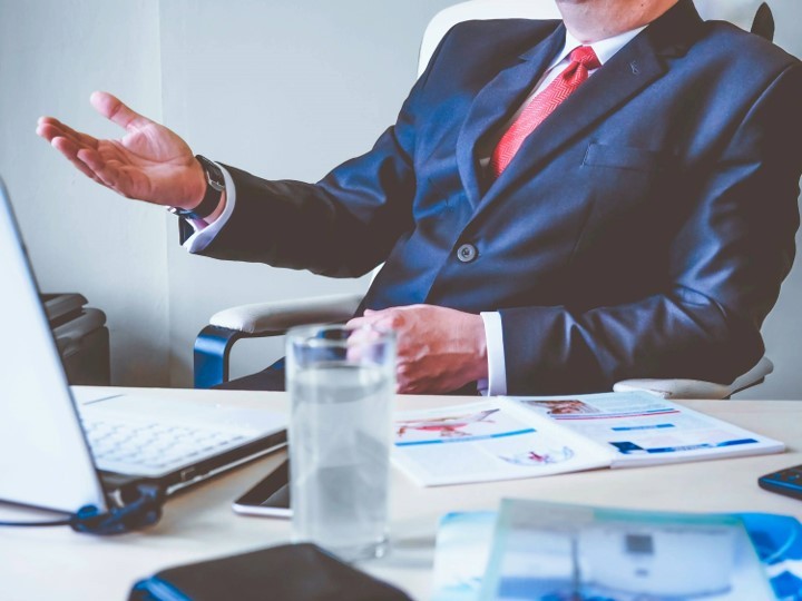 business man sitting at desk with laptop in front of him and a full glass of water and papers on the desk