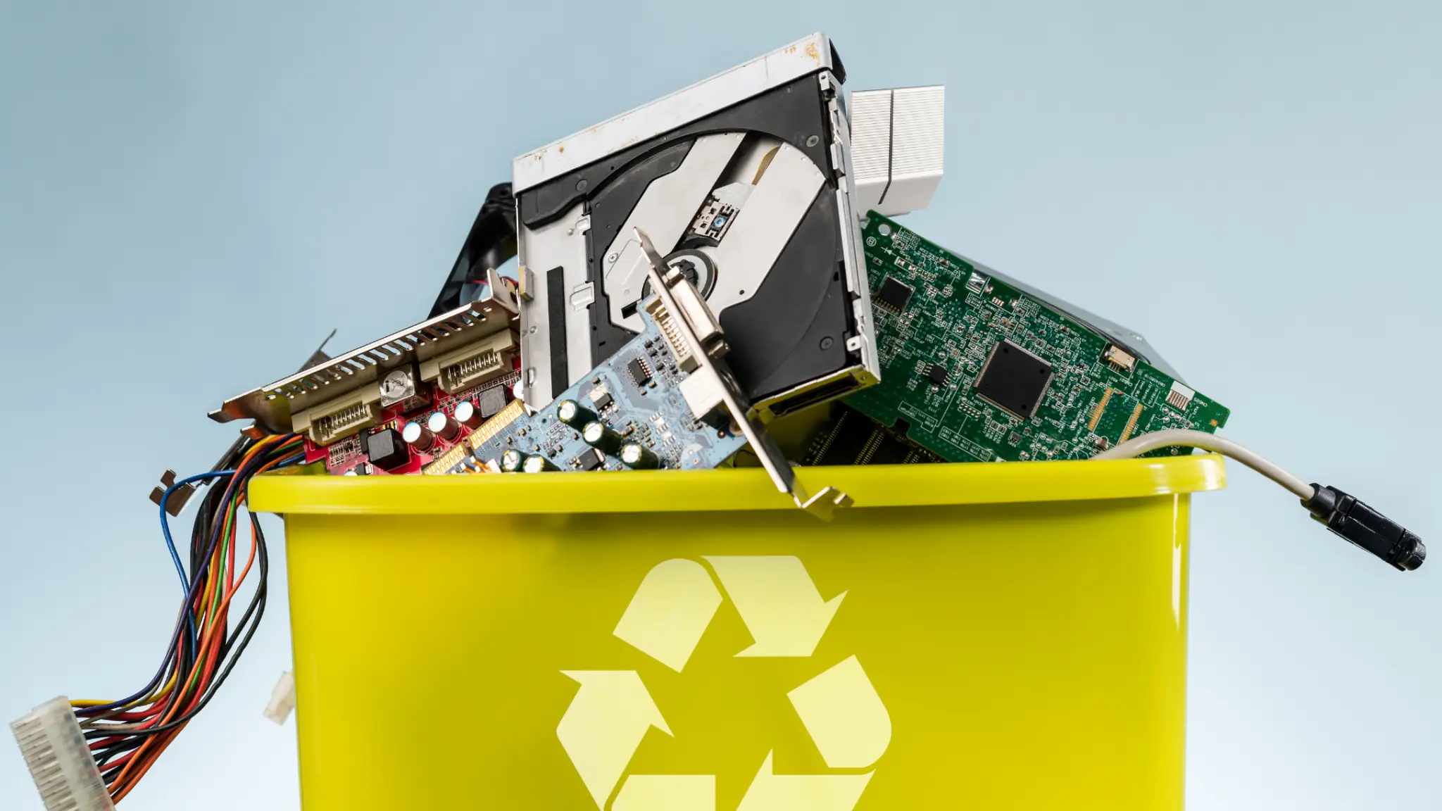 Electronic waste including hard drives, circuit boards, and cables placed in a yellow recycling bin with a recycle symbol