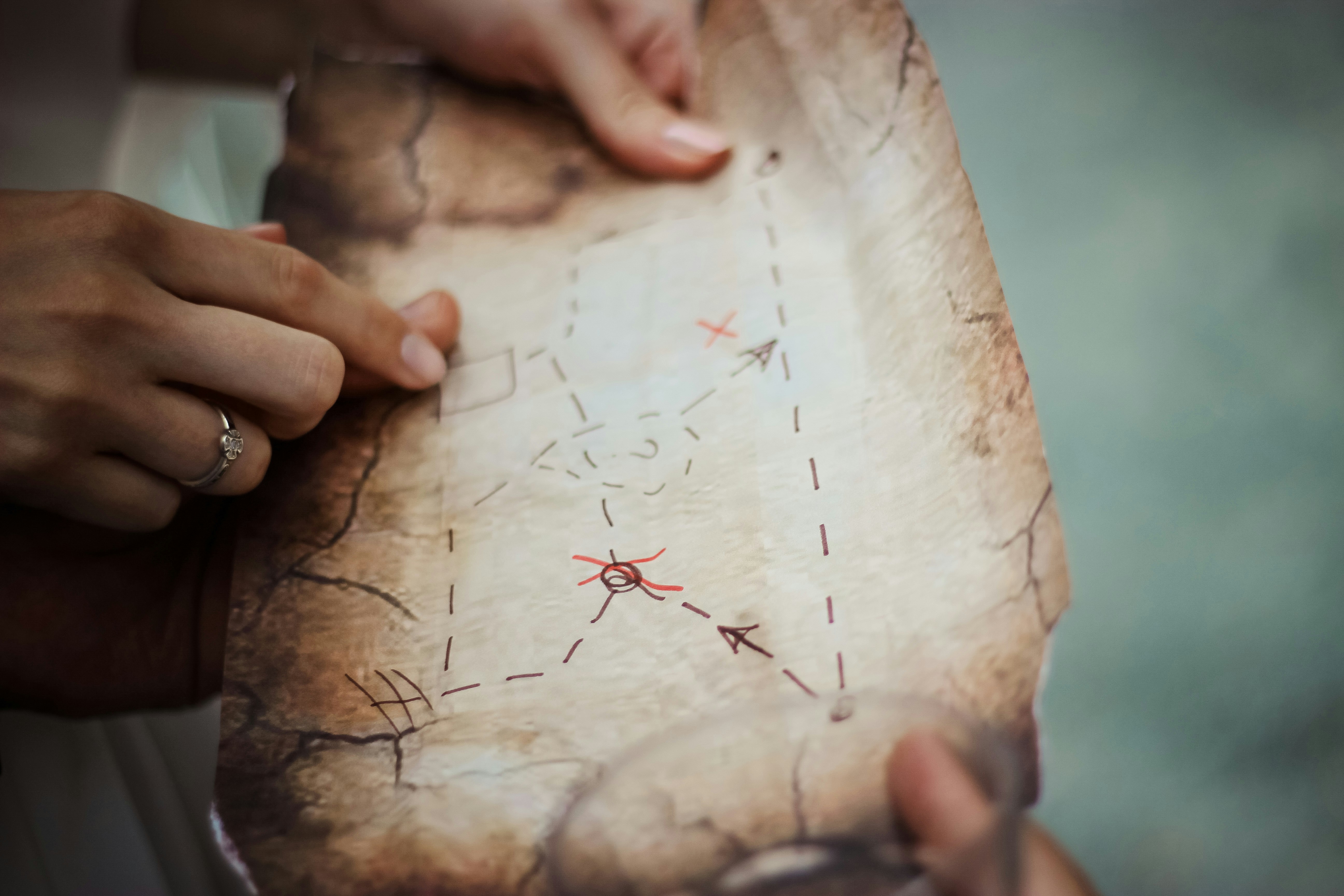 Close-up of hands holding and pointing to a marked path on a vintage treasure map, symbolizing the importance of aligning content goals to create a clear, impactful content strategy.