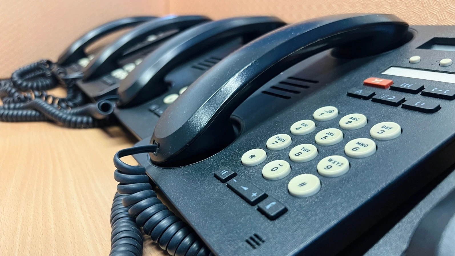 Sarawak, Malaysia - 17 December 2025: A row of black analog desktop telephones with coiled cords arranged on a wooden office desk. Corporate communication equipment and landline telecommunication systems.