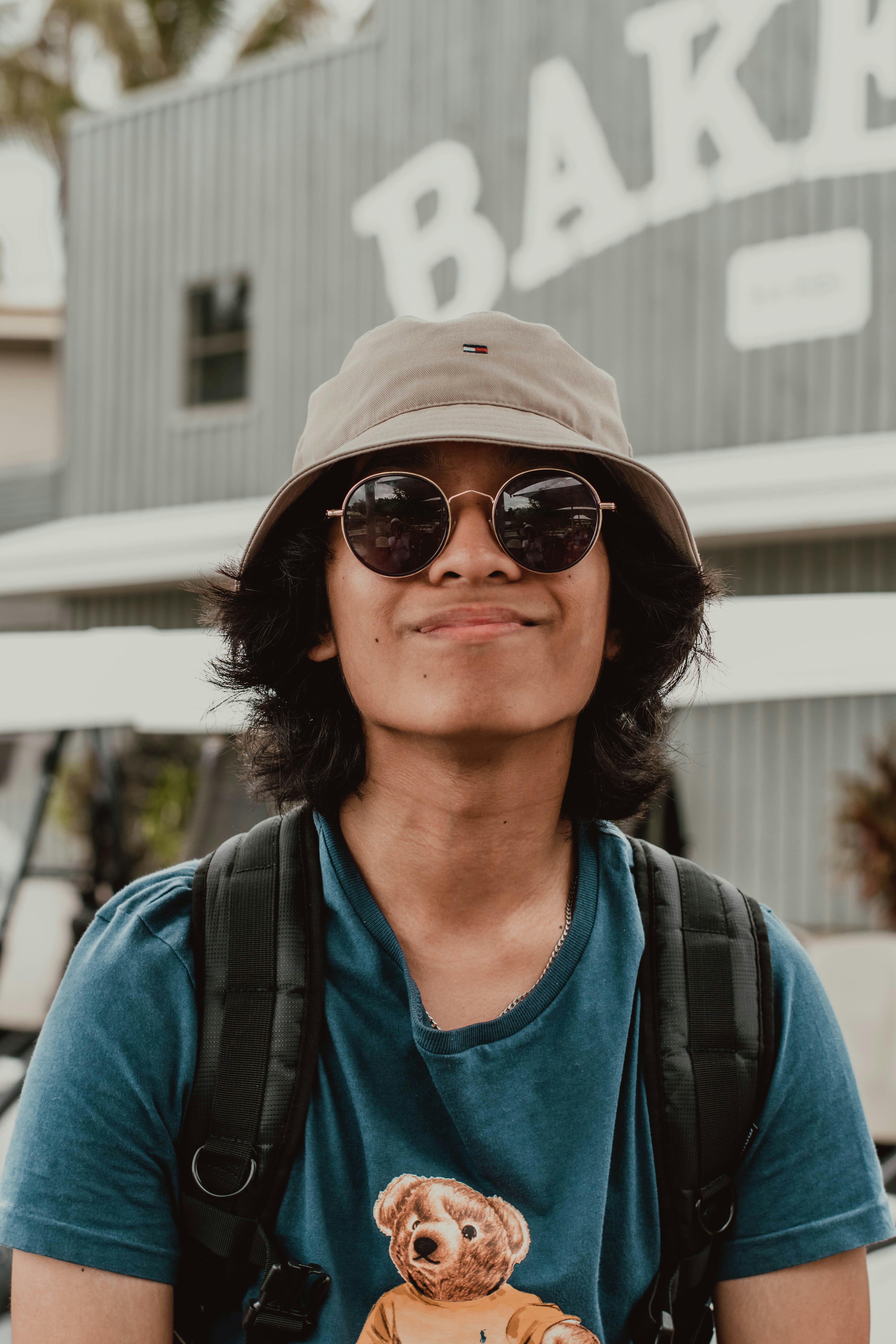 Young man in hat and sunglasses smiling near a bakery.