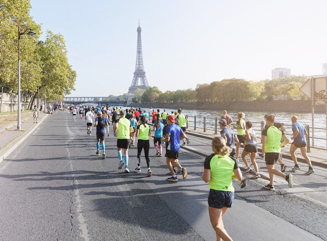 Groupe de coureurs en compétition sur les quais de Seine lors d'un événement, avec la Tour Eiffel visible à l'horizon.