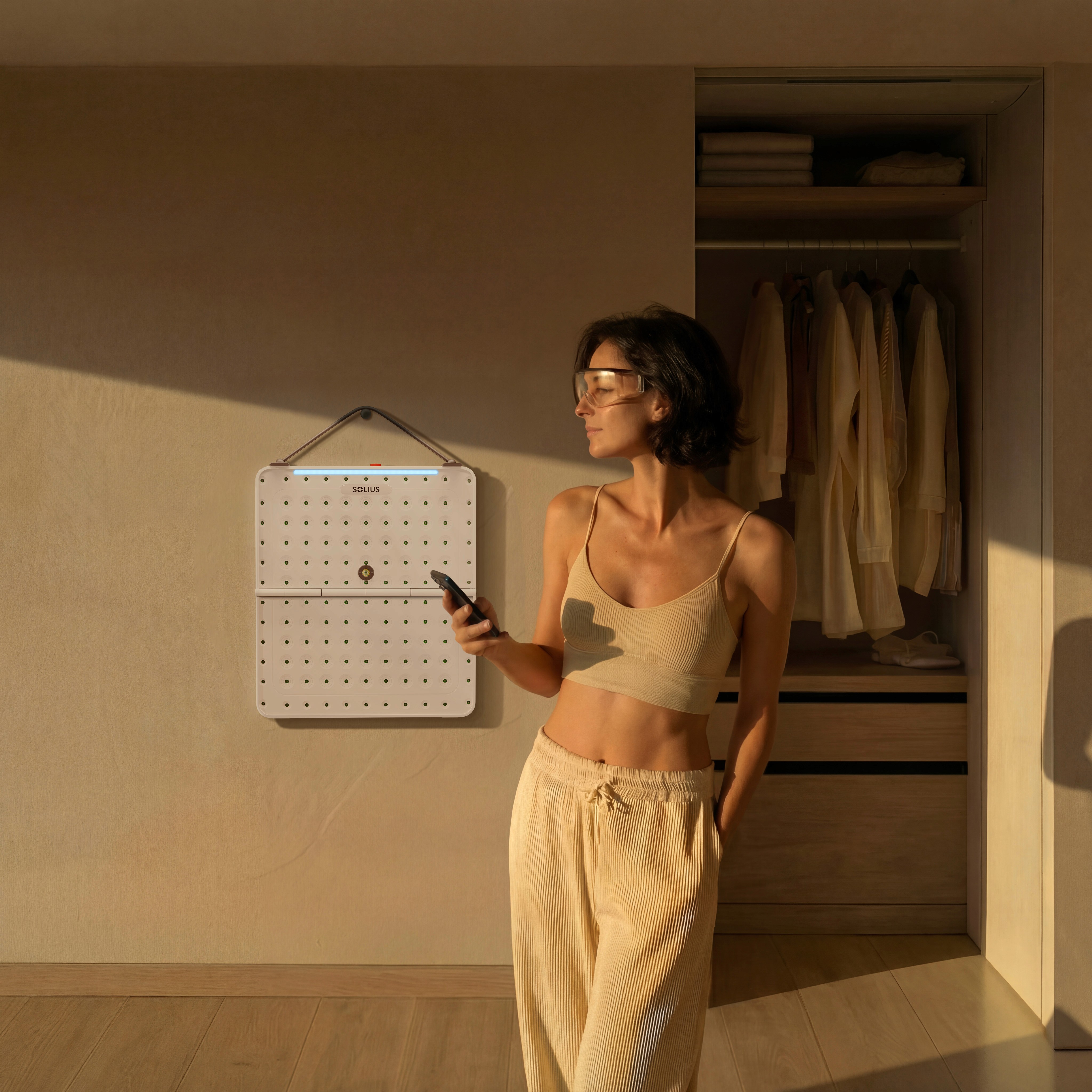 Woman wearing protective glasses holds a remote while standing next to a wall-mounted Solius light therapy panel in a softly lit, minimalist bedroom.