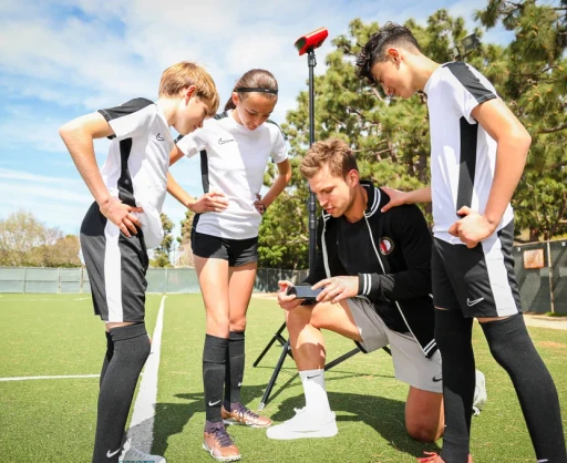 Soccer coach reviewing game footage on a smartphone with youth players, with a Reeplayer camera set up in the background