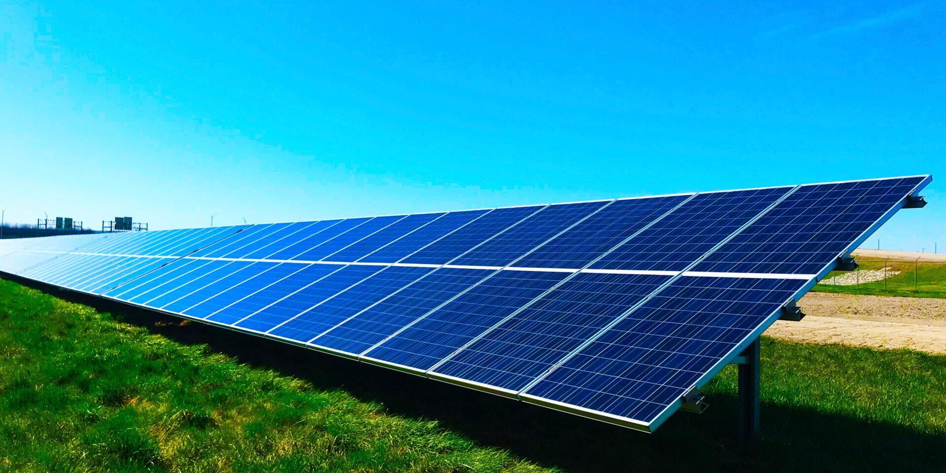 A large array of solar panels is installed on a grassy field under a clear blue sky, capturing renewable energy from sunlight.