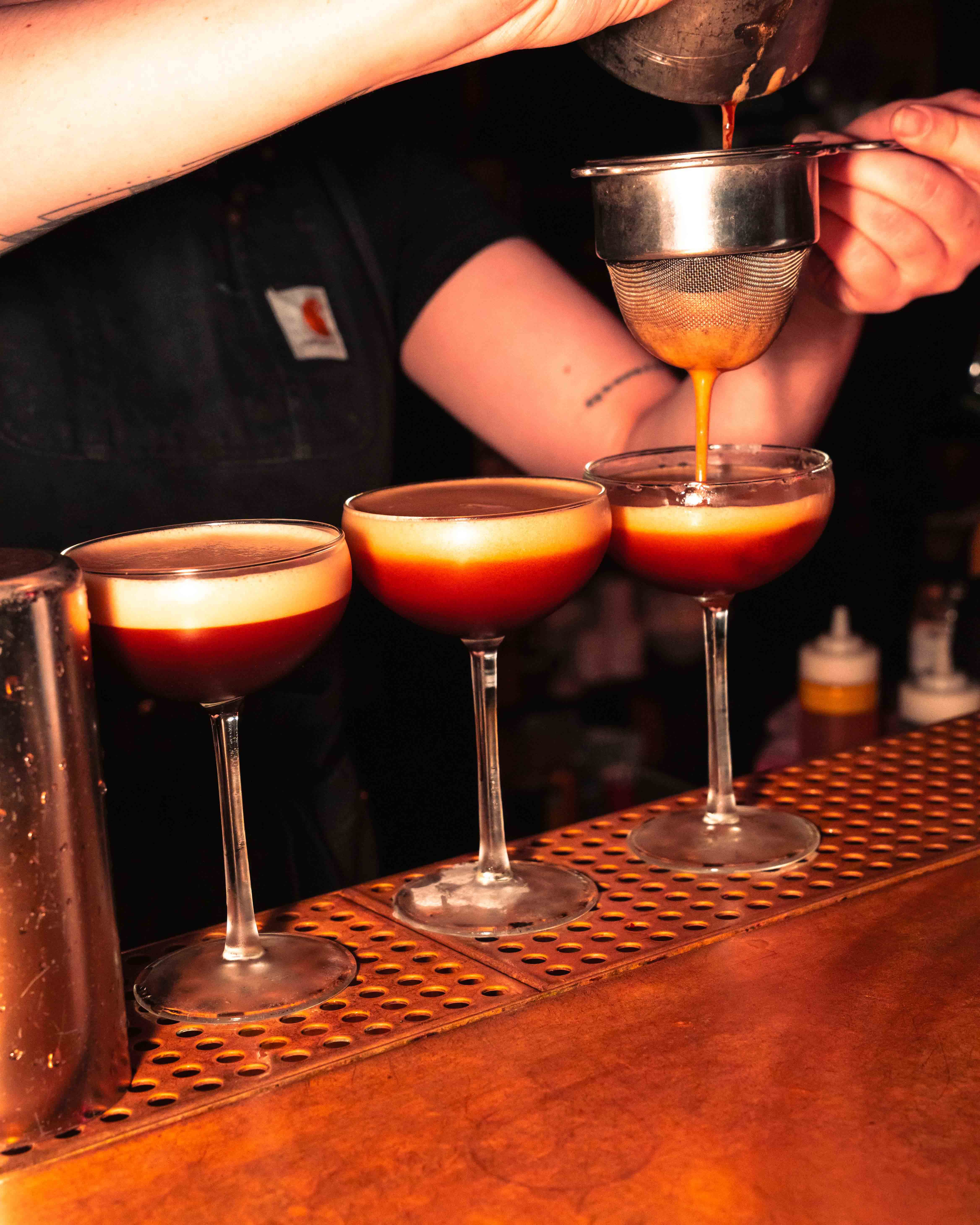 White plate with roasted carrots served on green sauce, topped with almonds and fresh herbs, held by a hand over a dark table.
