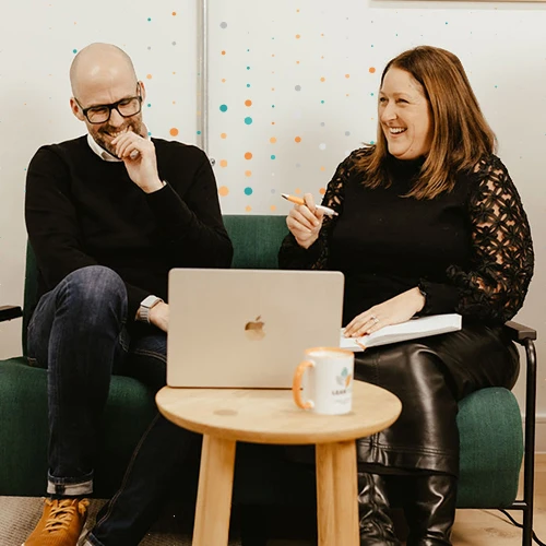 two people sitting infront of a laptop discussing