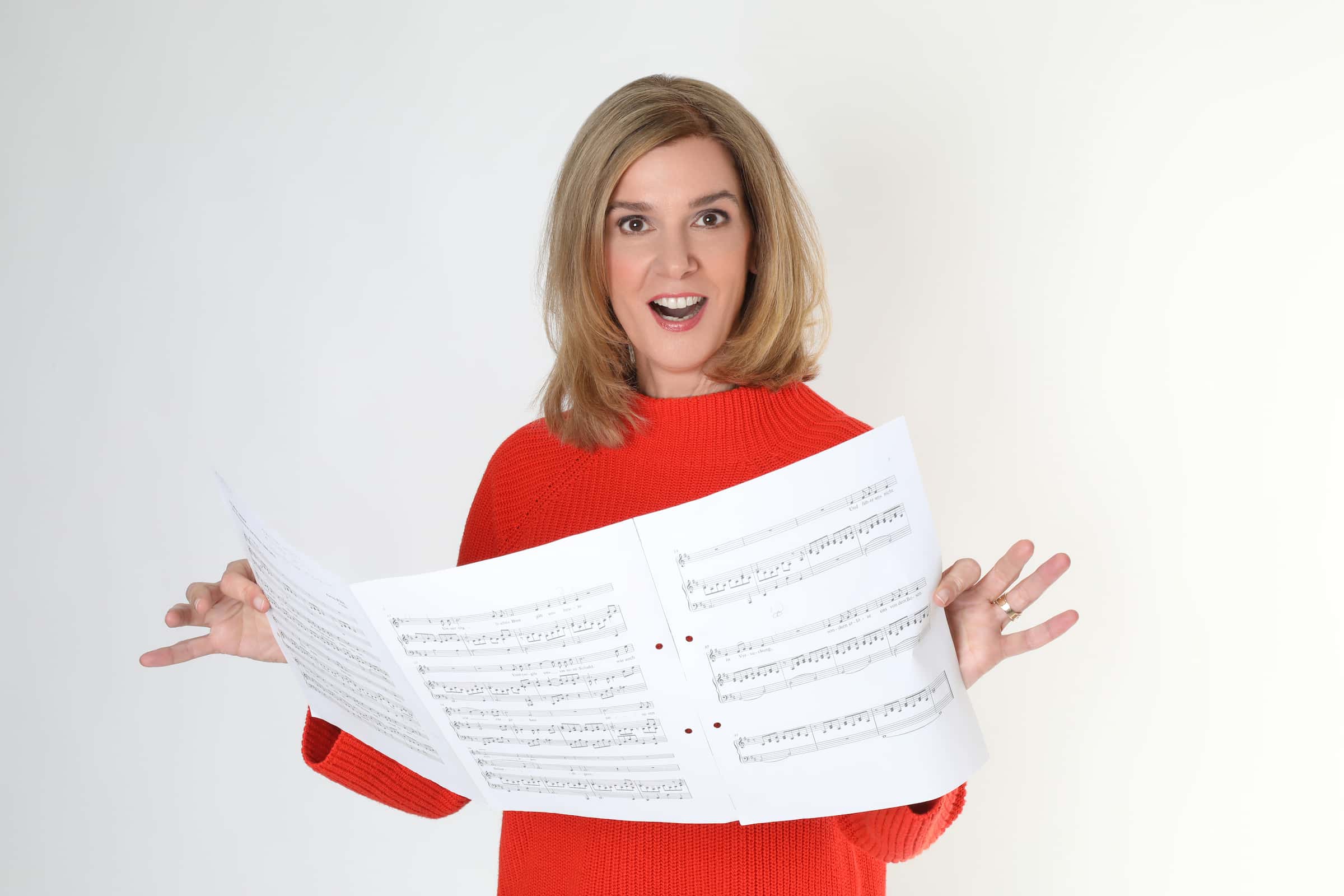 Danielle Zuber singt freudig und hält Notenblätter in der Hand. Promotion für den Online-Gesangskurs 'Singen lernen in 30 Tagen' von Singers Evolution.