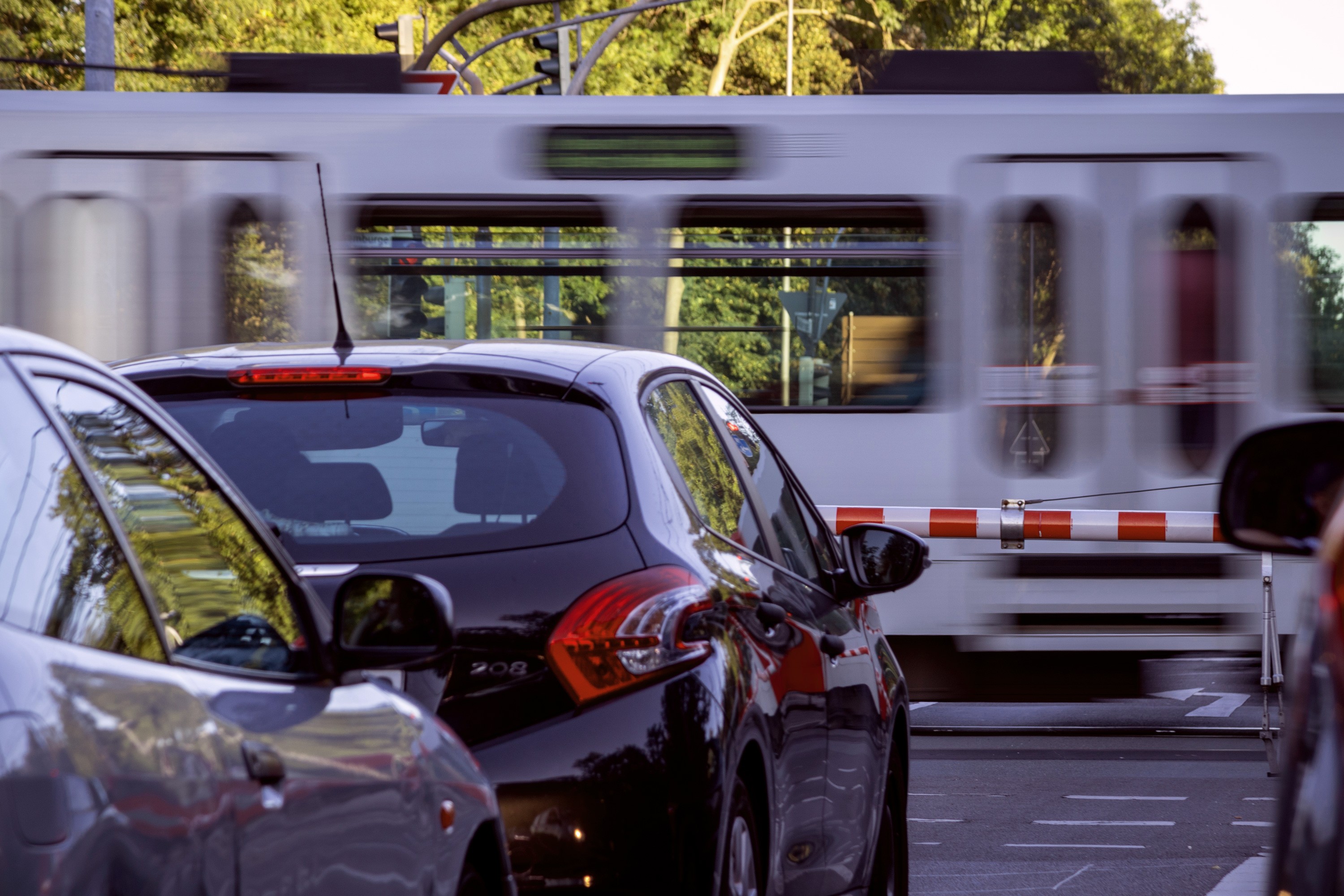 Autos im Stadtverkehr vor einer Schranke mit Straßenbahn