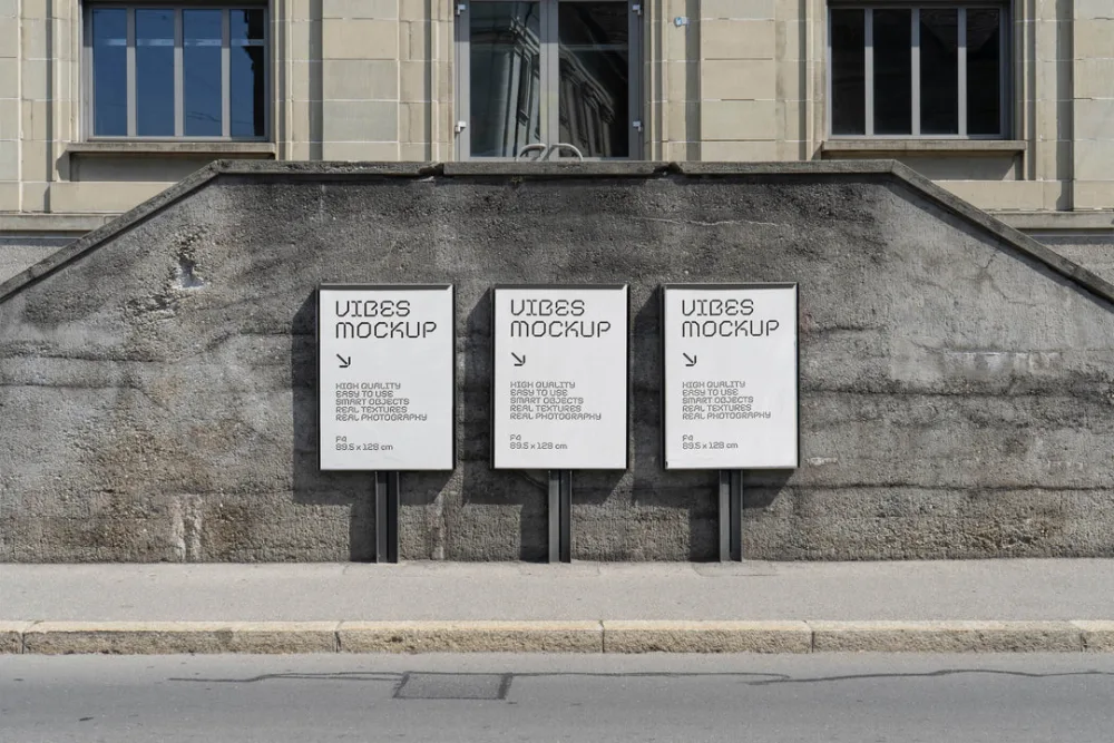 A trio of black poster mockups displayed on a textured concrete wall along a sidewalk, set against a historic building facade with large windows under natural daylight.