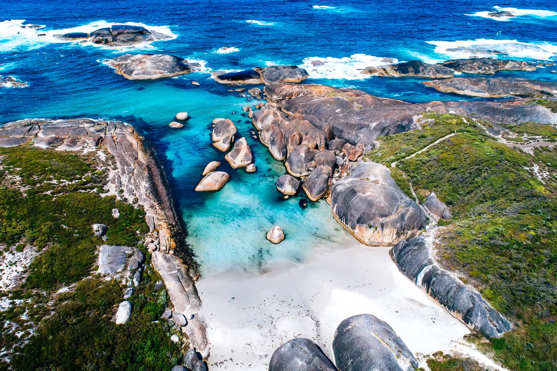Aerial of rounded granite boulders on a white beach with clear turquoise water and dark reef