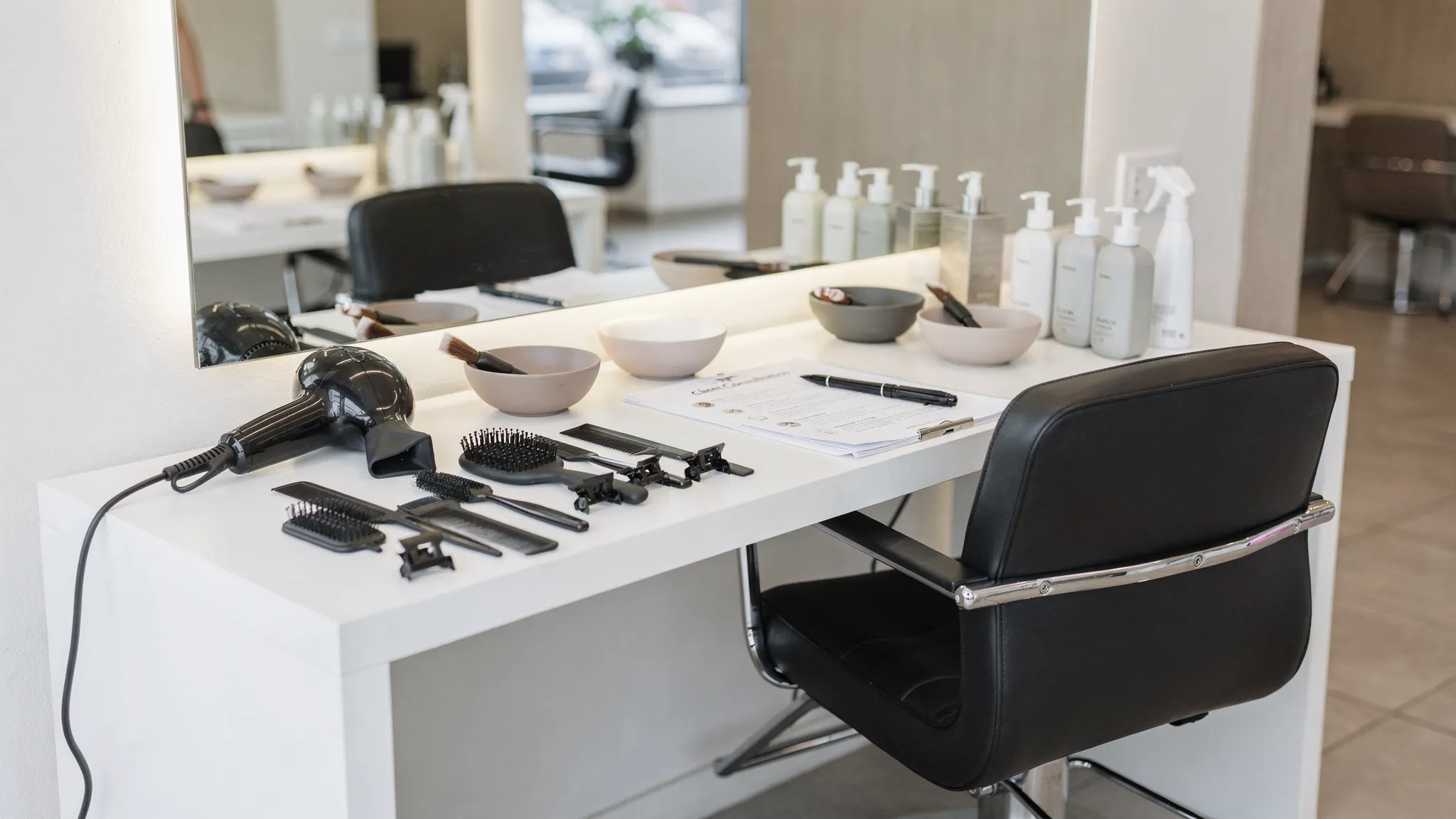 A modern salon chair with styling tools, color bowls, hair products, and a consultation card arranged neatly on a clean workstation.