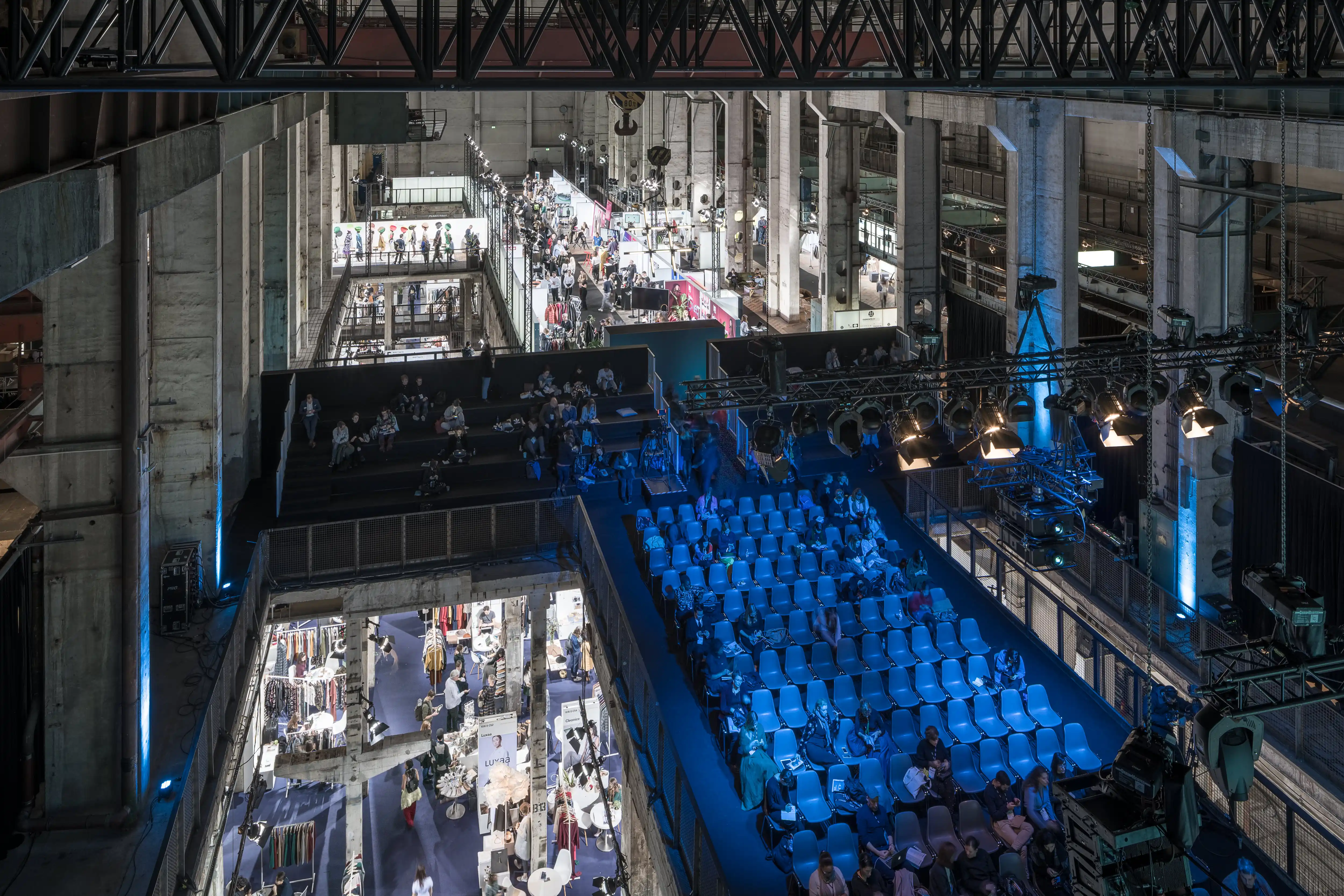 View from above onto the blue-lit conference seating and surrounding fashion exhibition levels at NEONYT in Kraftwerk Berlin.