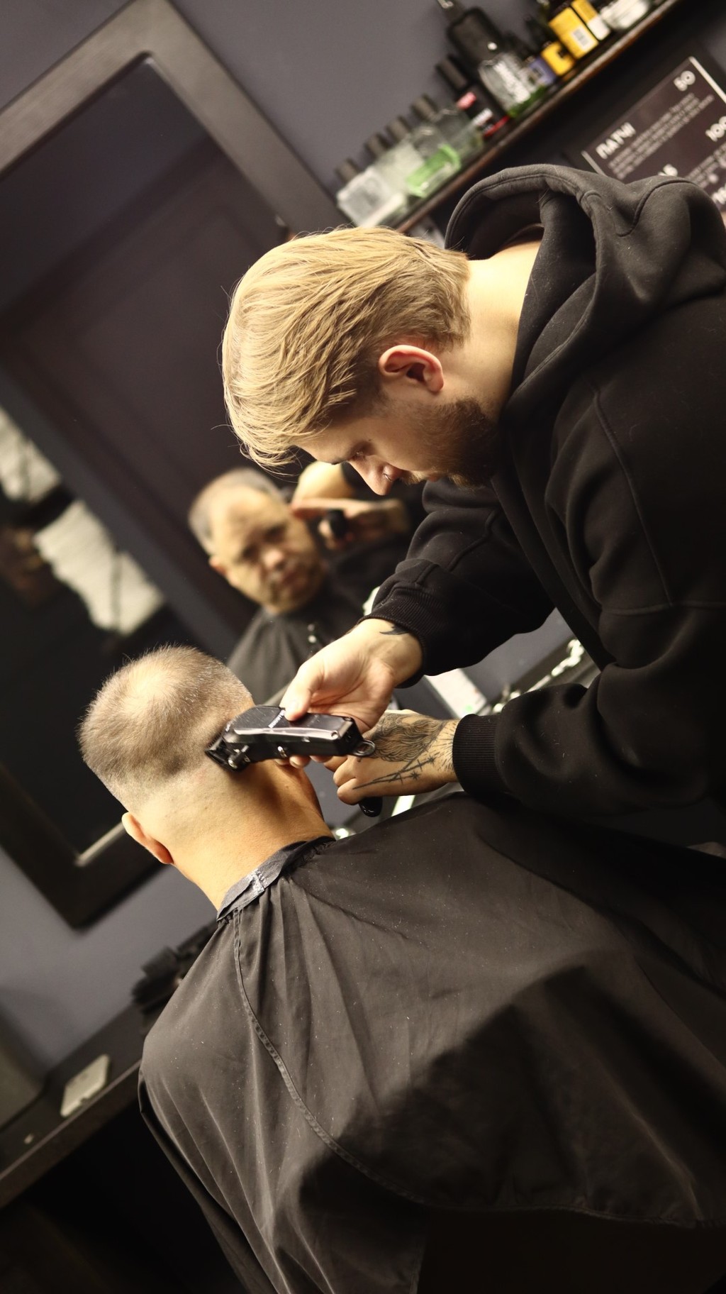 A barber cuts the hair of a client in a salon, both focused on the haircut process.