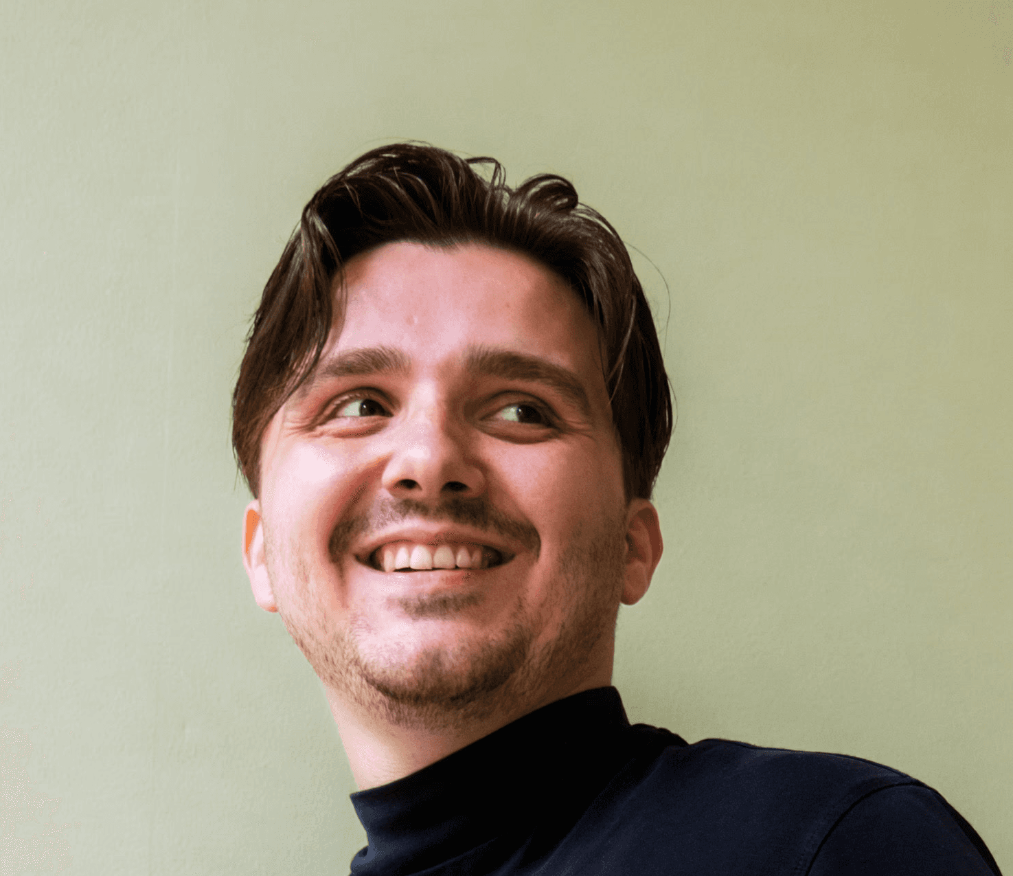 Profilfoto einer lächelnden Person in schwarzer Kleidung vor einem grünen Hintergrund