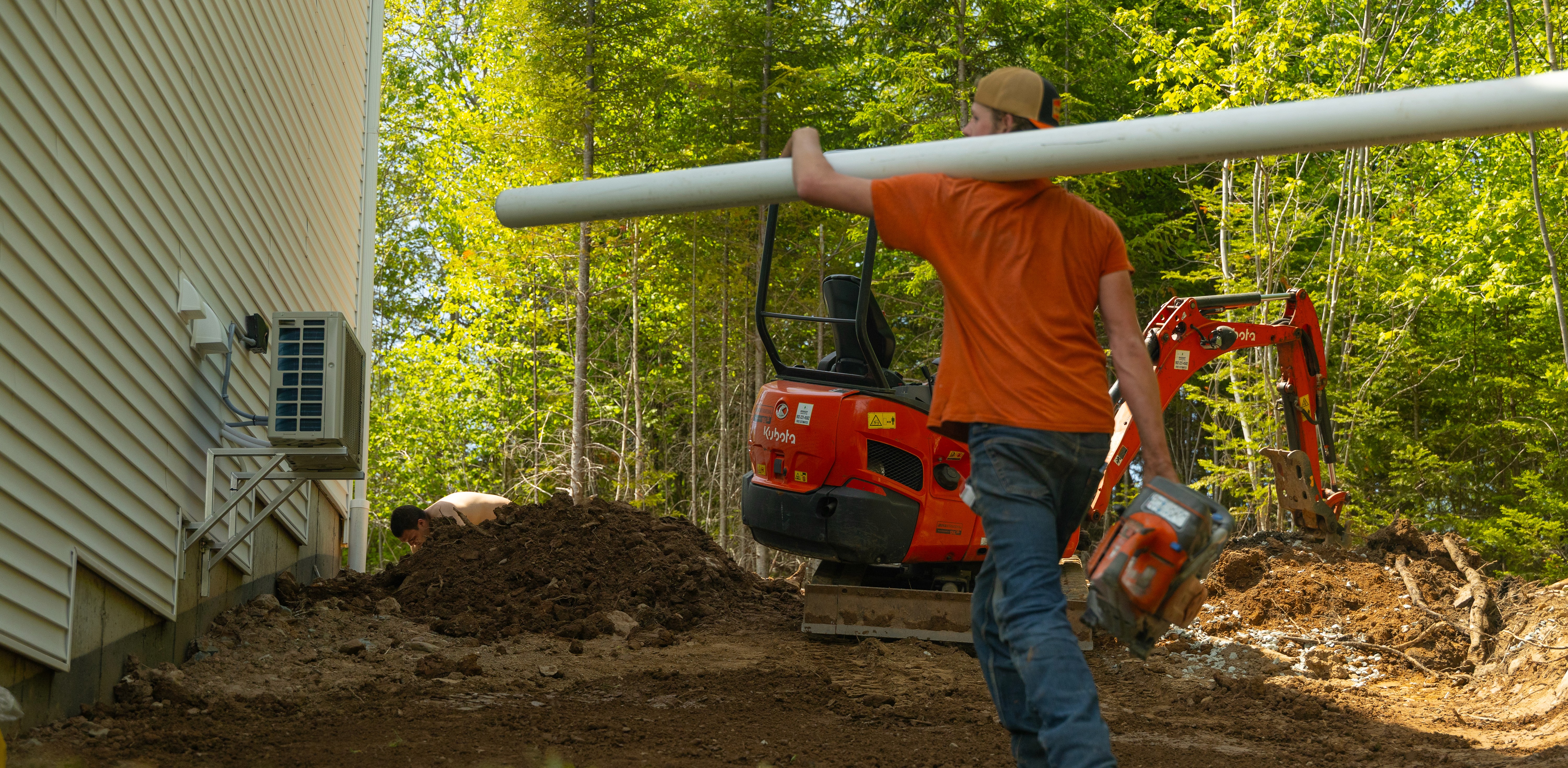 Doucet Landscaping crew member carrying drainage pipe with a Kubota excavator on a site preparation job in Halifax, Nova Scotia