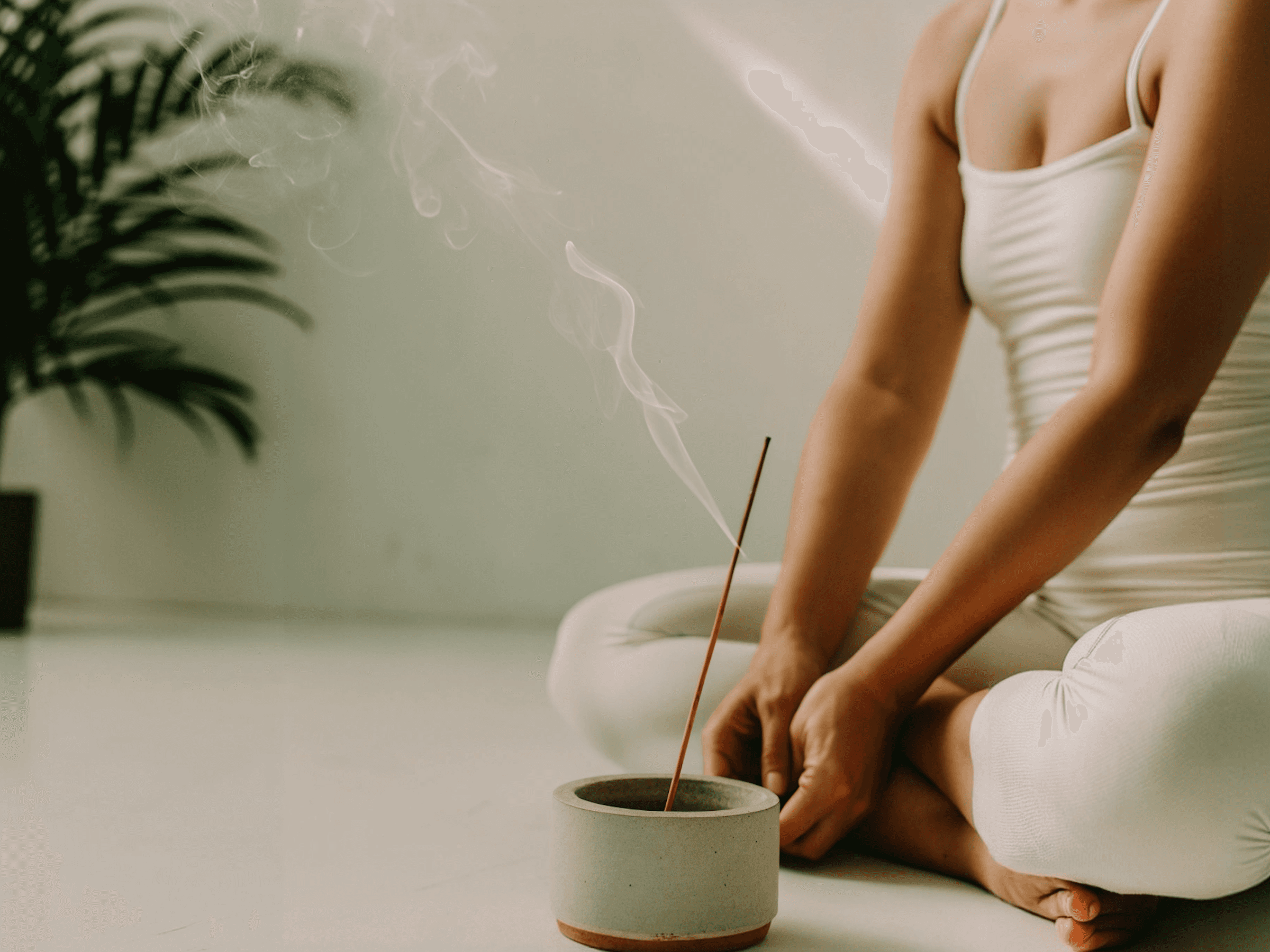 Person meditating in white clothing with a burning incense stick in a concrete bowl
