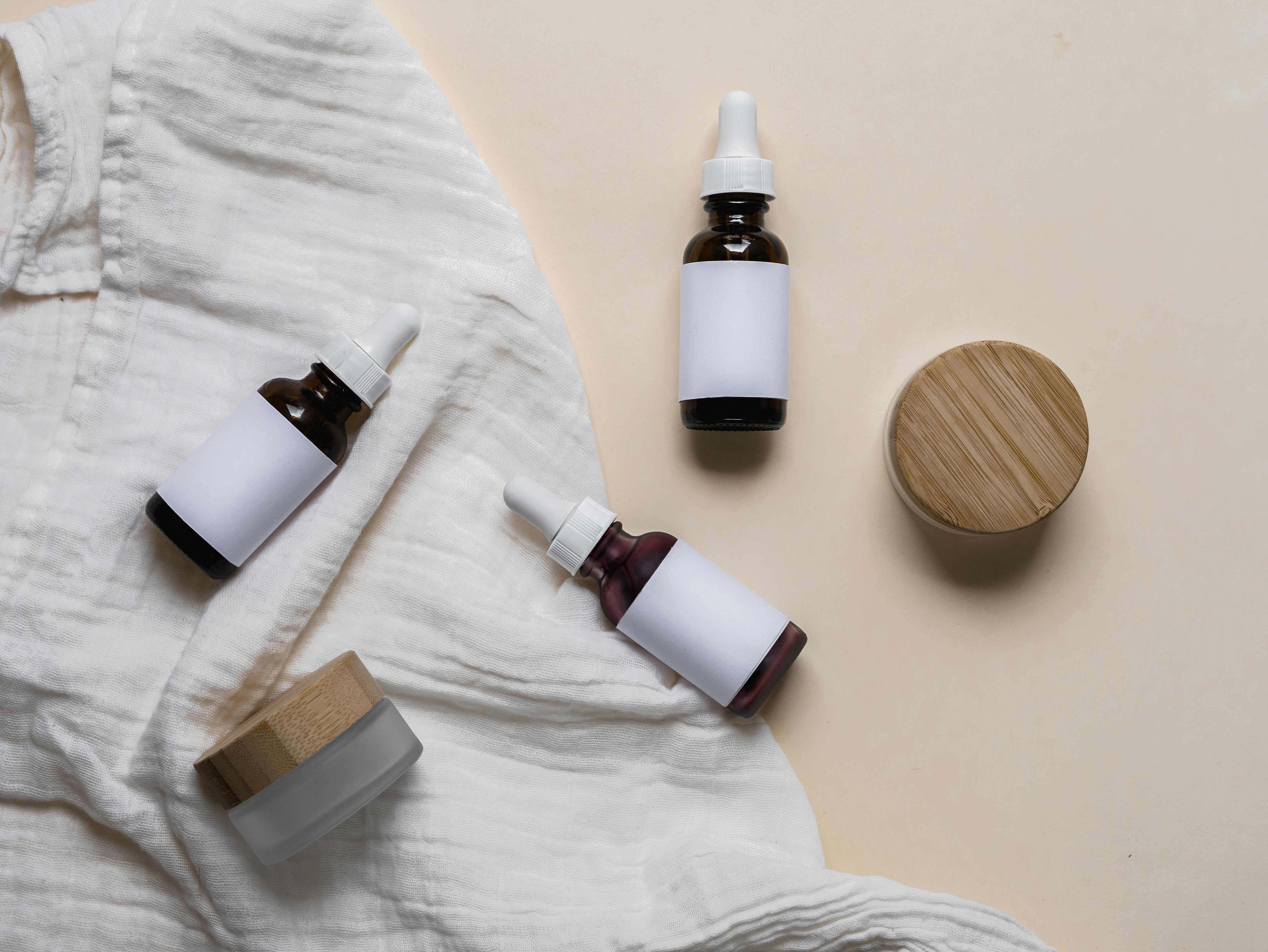 Spa products: skincare serum bottles, cream jars, and soap bar on white cloth. Natural beauty products, self-care concept.