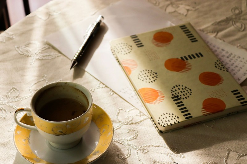 Patterned notebook, pen and a cup of tea on a lace tablecloth